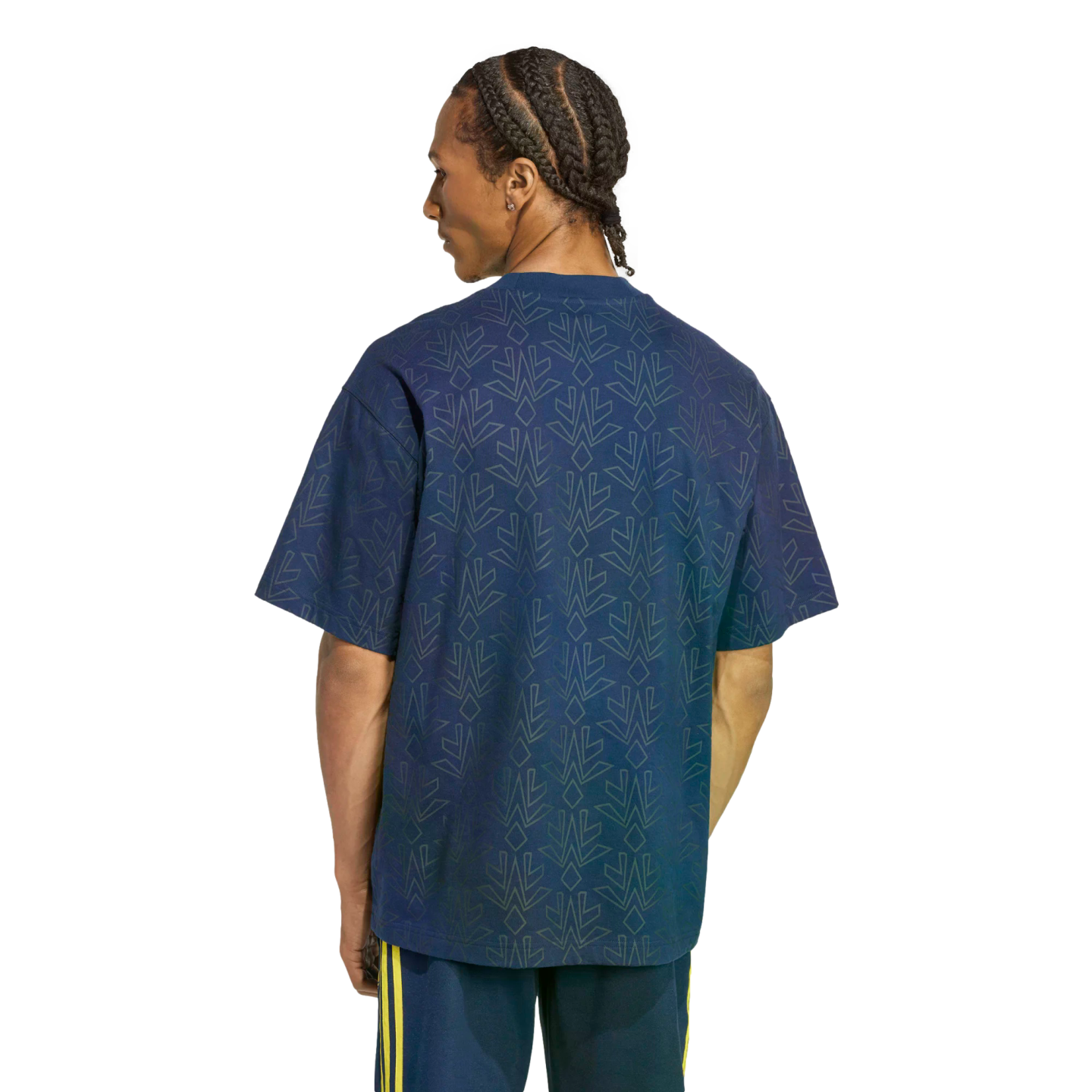 Back view of a man with braided hair wearing a dark blue t-shirt with a geometric pattern and navy shorts with yellow stripes against a solid black background.