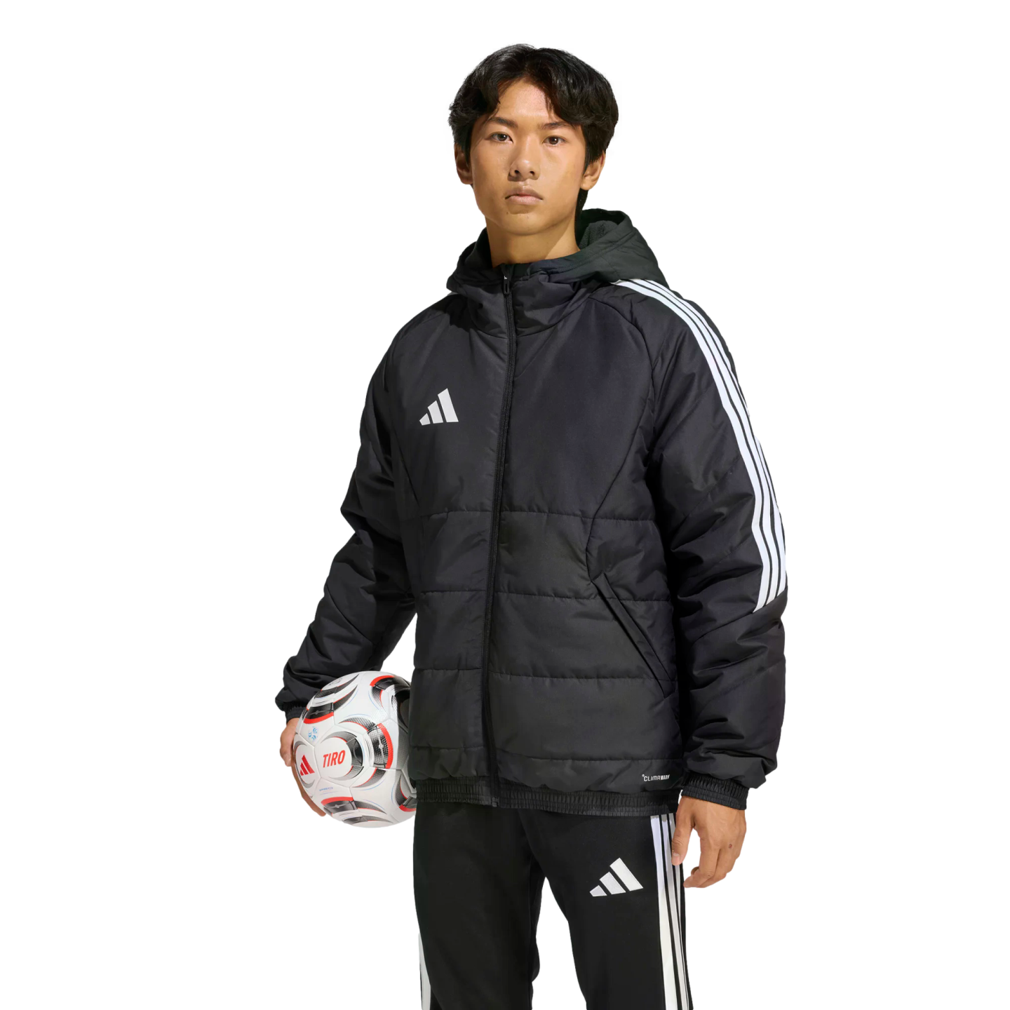 Man wearing a black Adidas puffer jacket and tracksuit pants, holding a soccer ball against a solid black background.