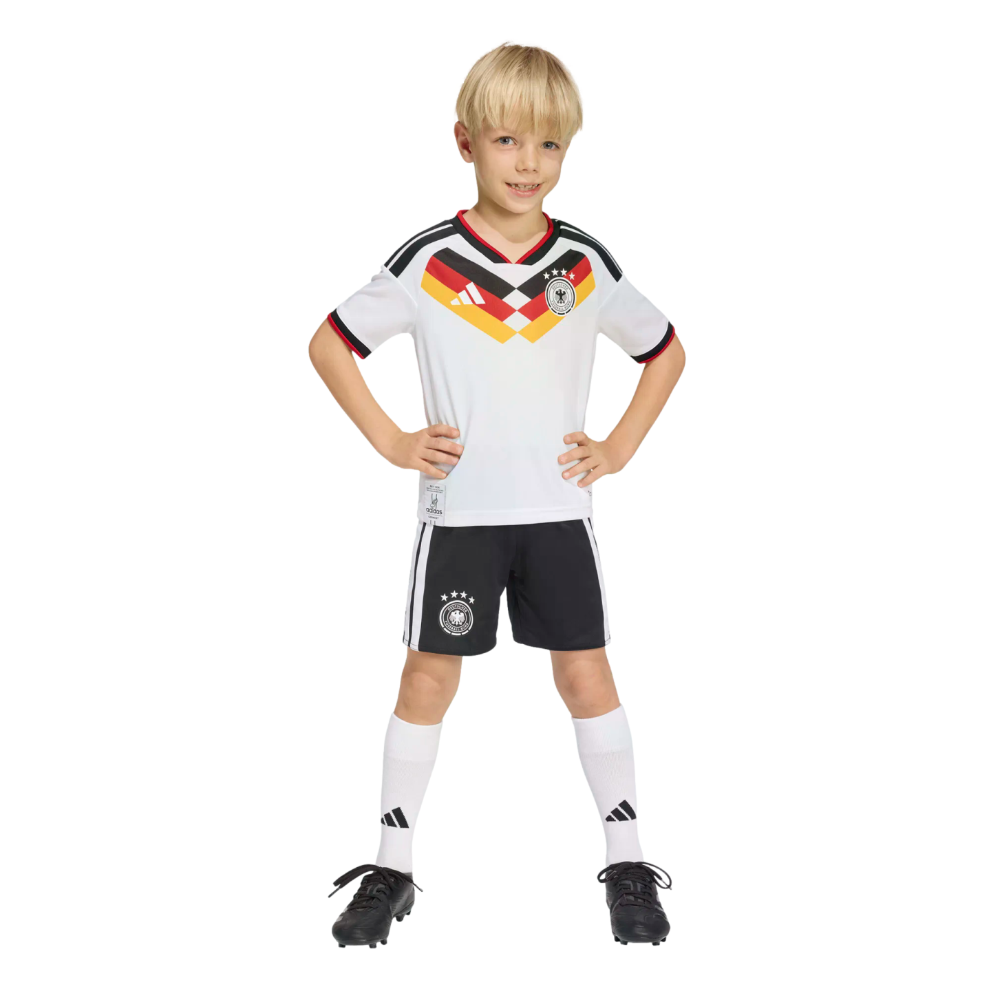 A smiling young boy wearing a Germany national team soccer kit, standing with hands on hips against a black background.