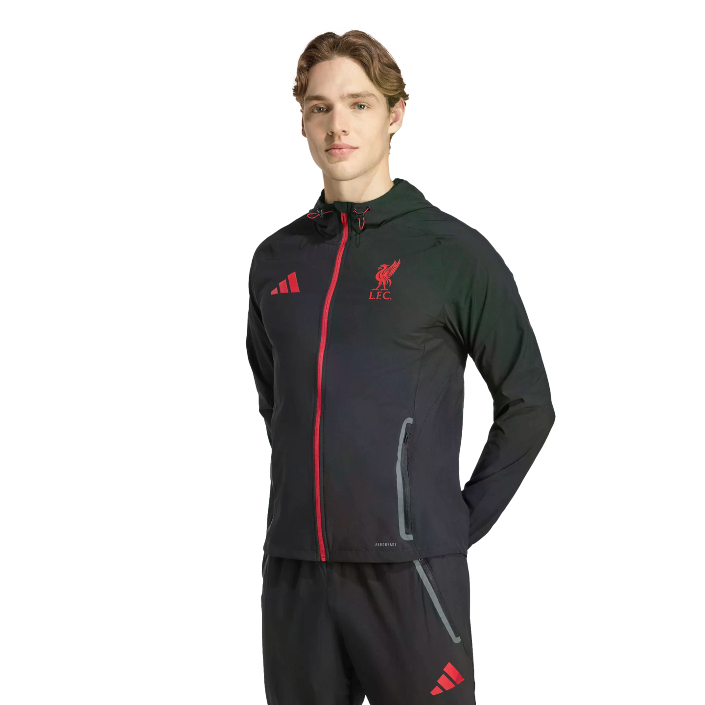 A man wearing a black Adidas Liverpool F.C. training jacket and pants with red logos and detailing, standing against a solid black background.
