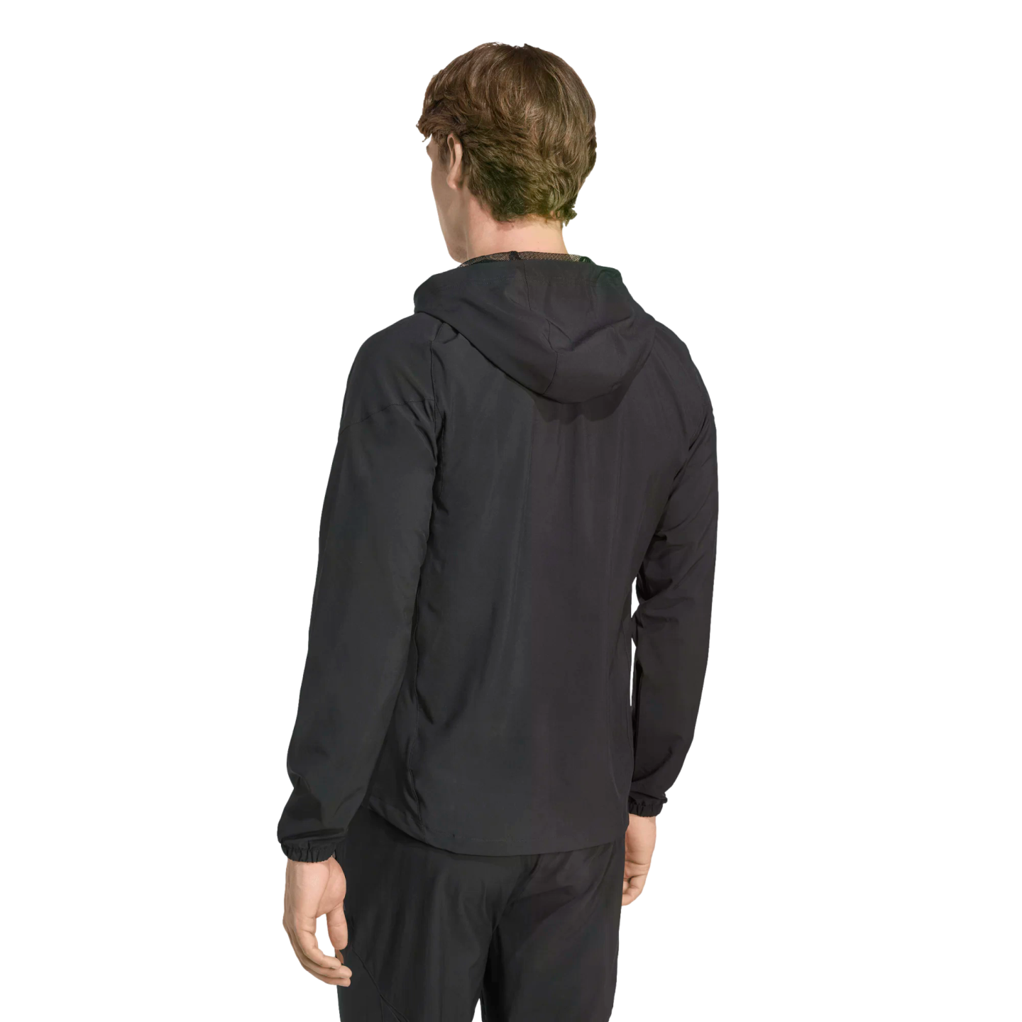 Rear view of a man with short brown hair wearing a black hooded jacket and matching pants against a solid black background.