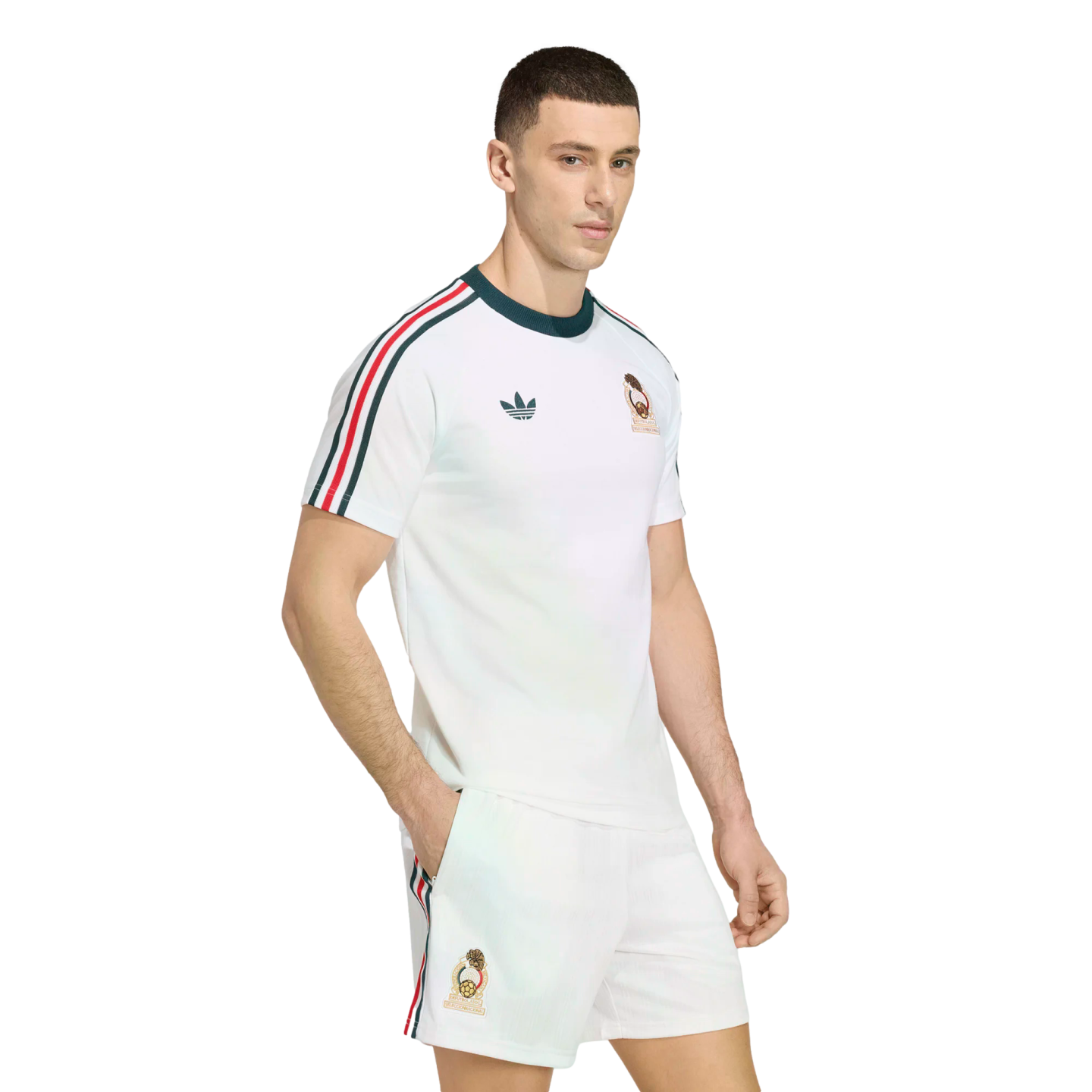 A man models a white Adidas football kit with green and red striped accents on the sleeves and shorts, featuring a gold team crest, against a solid black background.