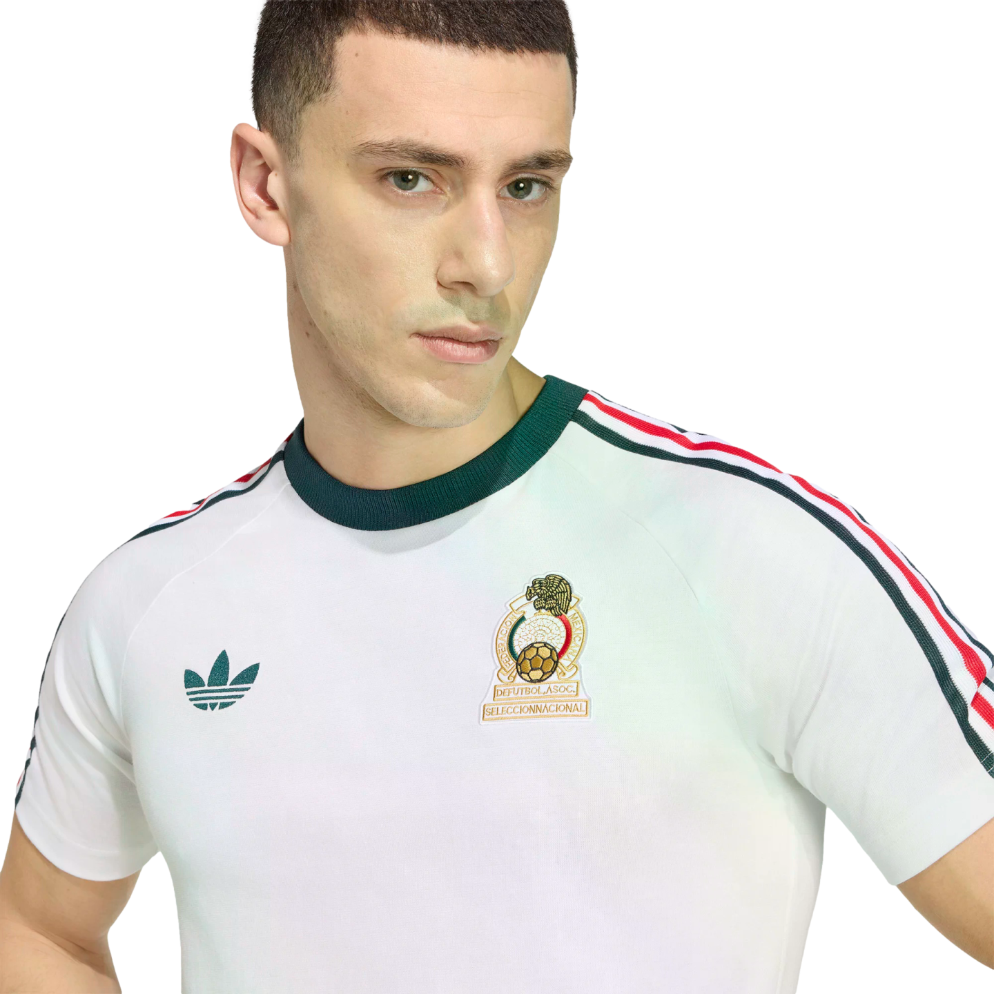 A close-up of a young man wearing a white retro Mexico National Team t-shirt by Adidas. The shirt features a dark green crew neck, a green Adidas Trefoil logo on the right, and the Mexican National Team crest on the left. Three stripes in green, white, an