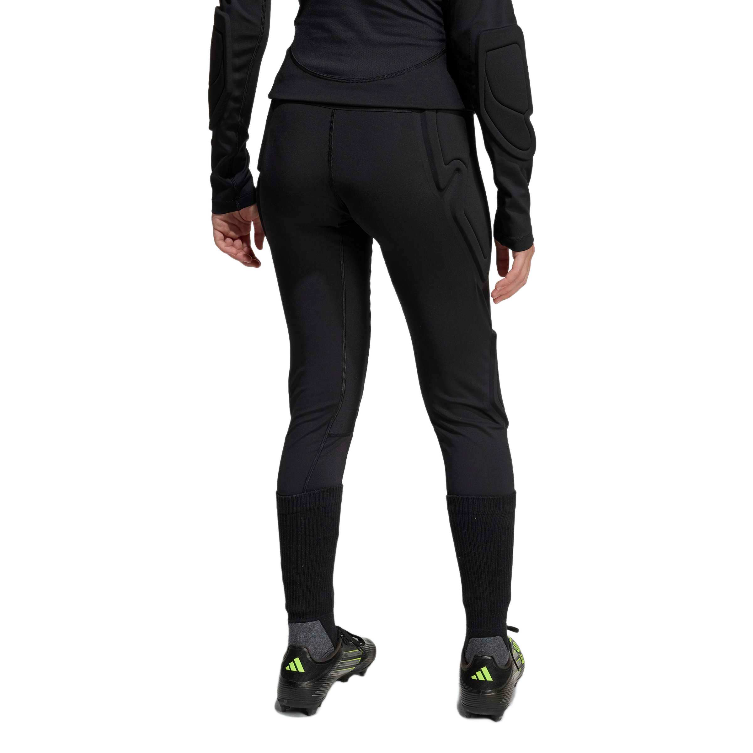 Rear view of a person wearing black padded athletic leggings, a long-sleeve padded top, tall black socks, and soccer cleats against a plain white background.