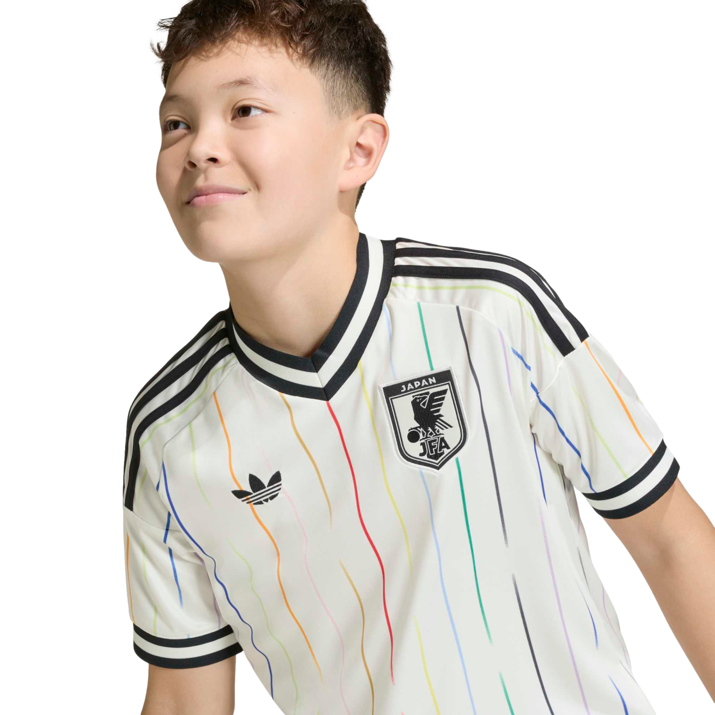A young person smiling in a white Adidas Japan football jersey with vertical rainbow stripes, set against a solid black background.