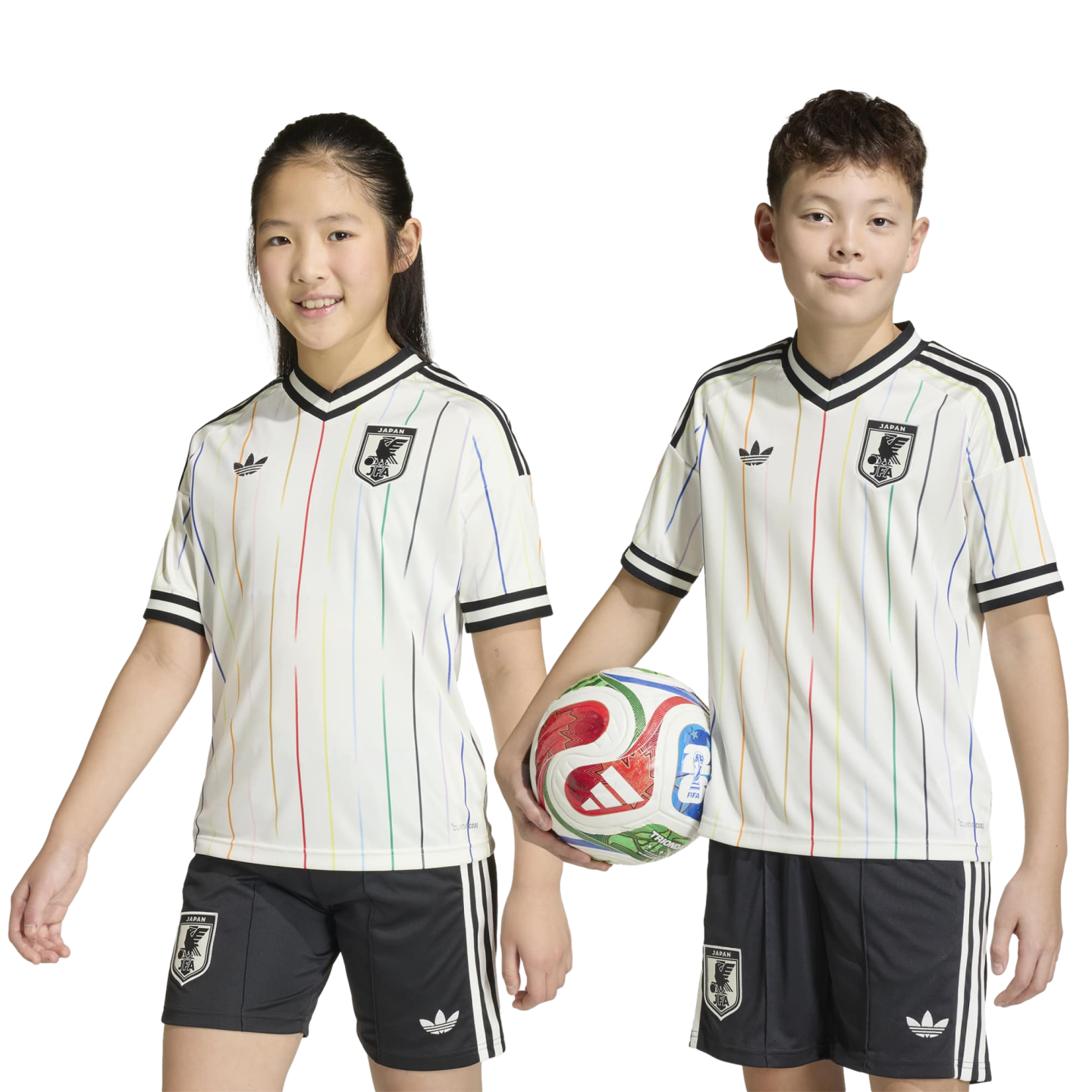 Two smiling children pose in matching white Japan soccer jerseys with colorful stripes and black shorts. The boy holds a soccer ball.