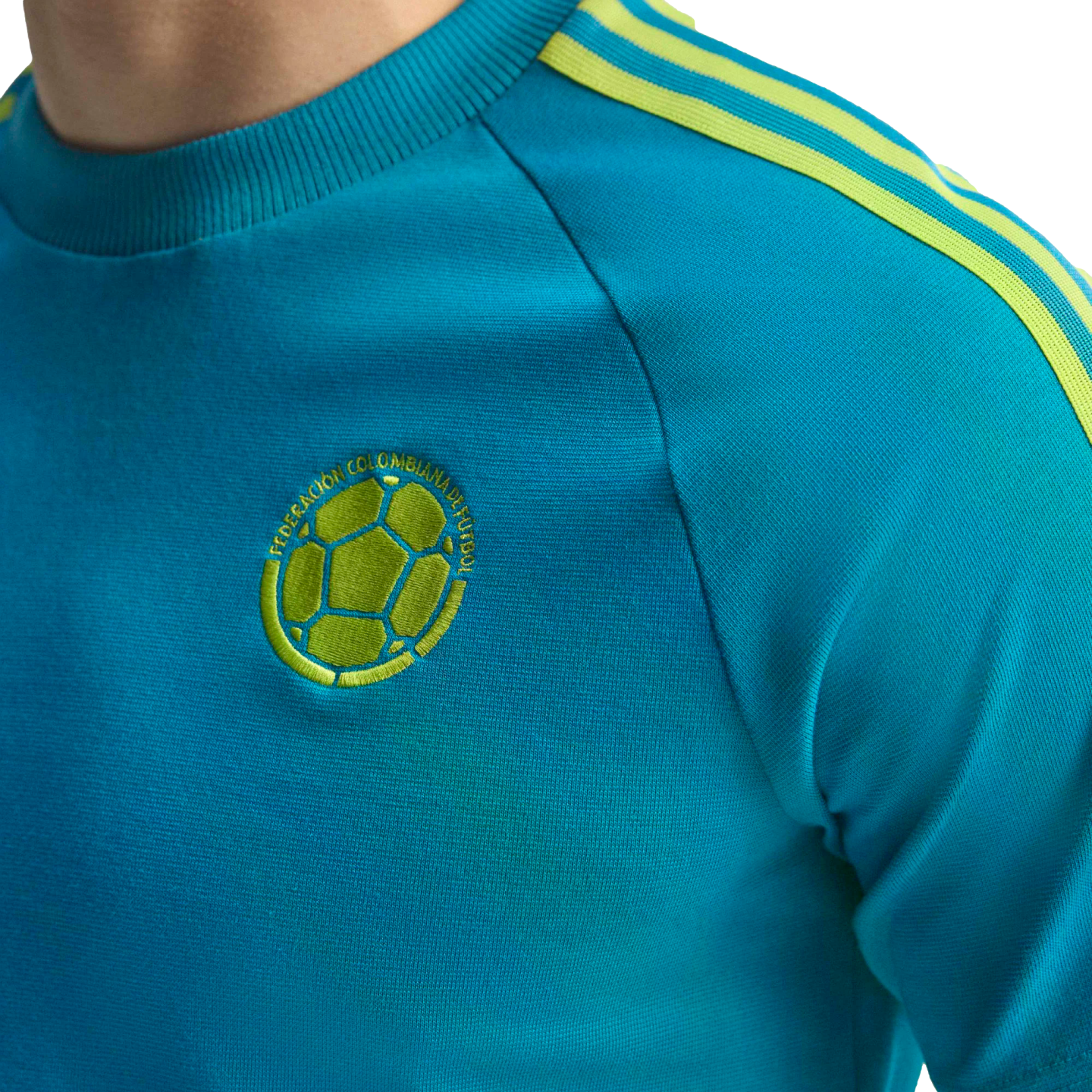 Turquoise shirt with three neon green shoulder stripes and an embroidered Colombian Football Federation logo on the chest.