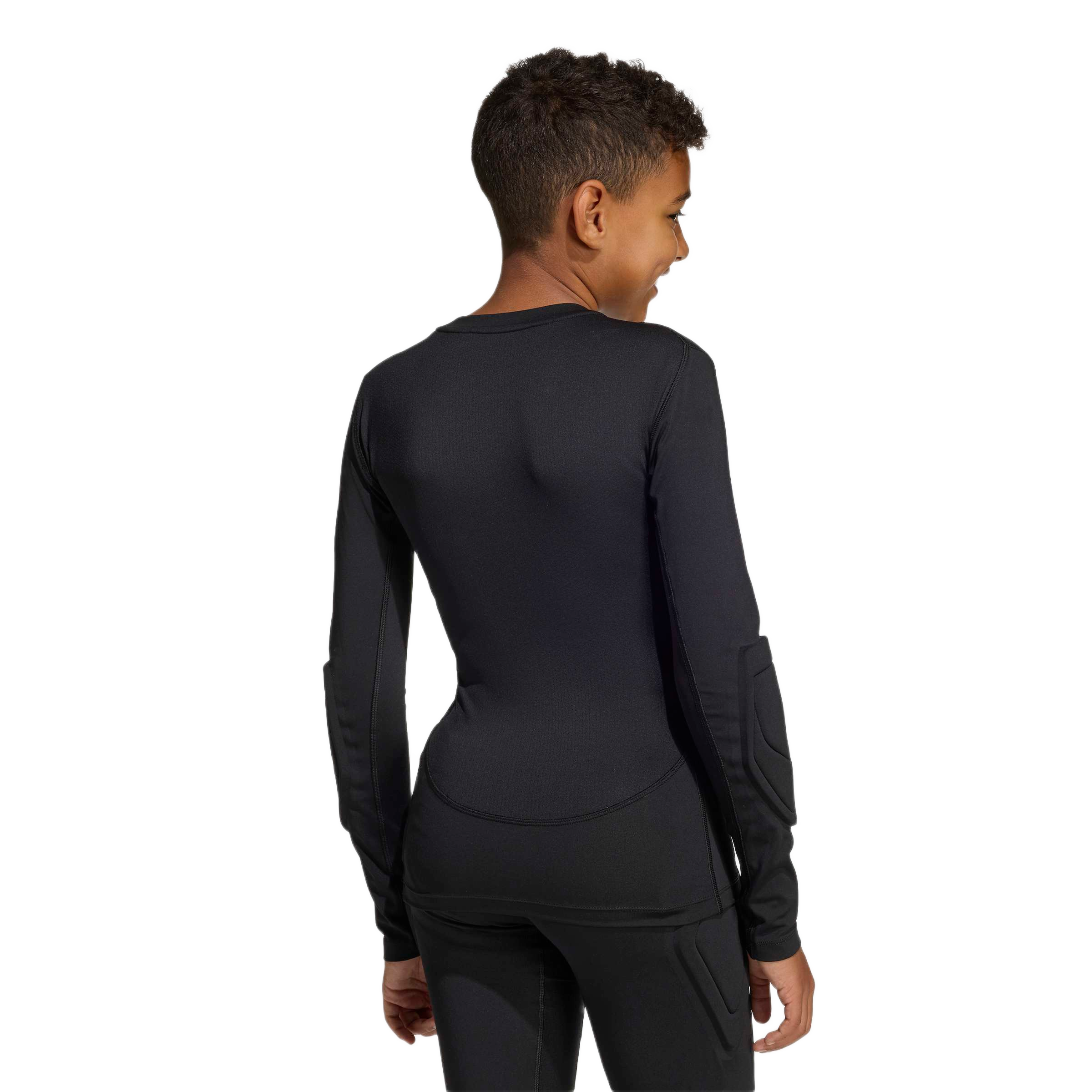 Back view of a youth in a black long-sleeved padded athletic shirt and matching pants, smiling over their shoulder against a plain background.