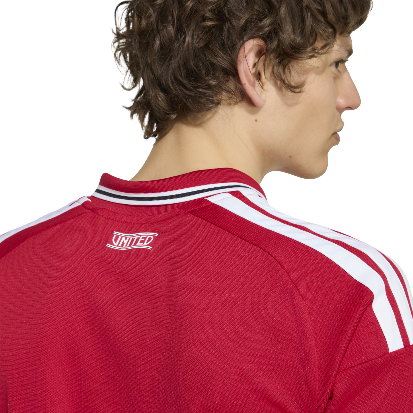 Close-up from behind of a man wearing a red jersey with three white stripes on the shoulder and "UNITED" printed on the back neck.