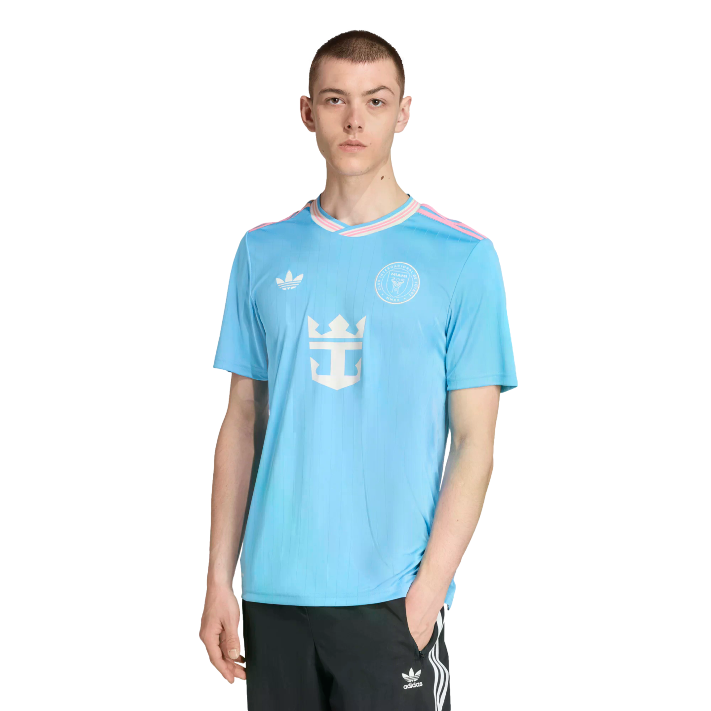 A man models a light blue Inter Miami CF soccer jersey with pink accents and black Adidas pants against a white background.