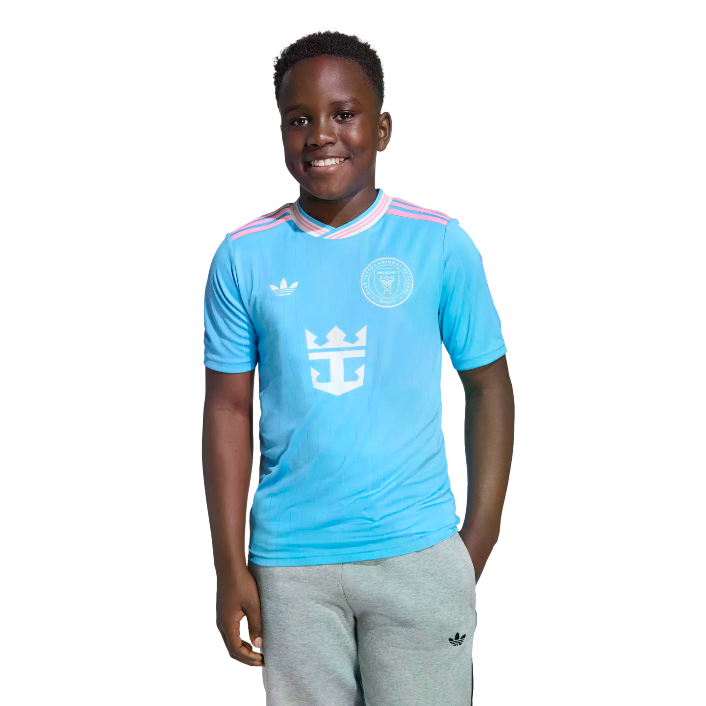 Smiling young boy wearing a light blue Inter Miami CF soccer jersey and gray sweatpants, isolated on a white background.