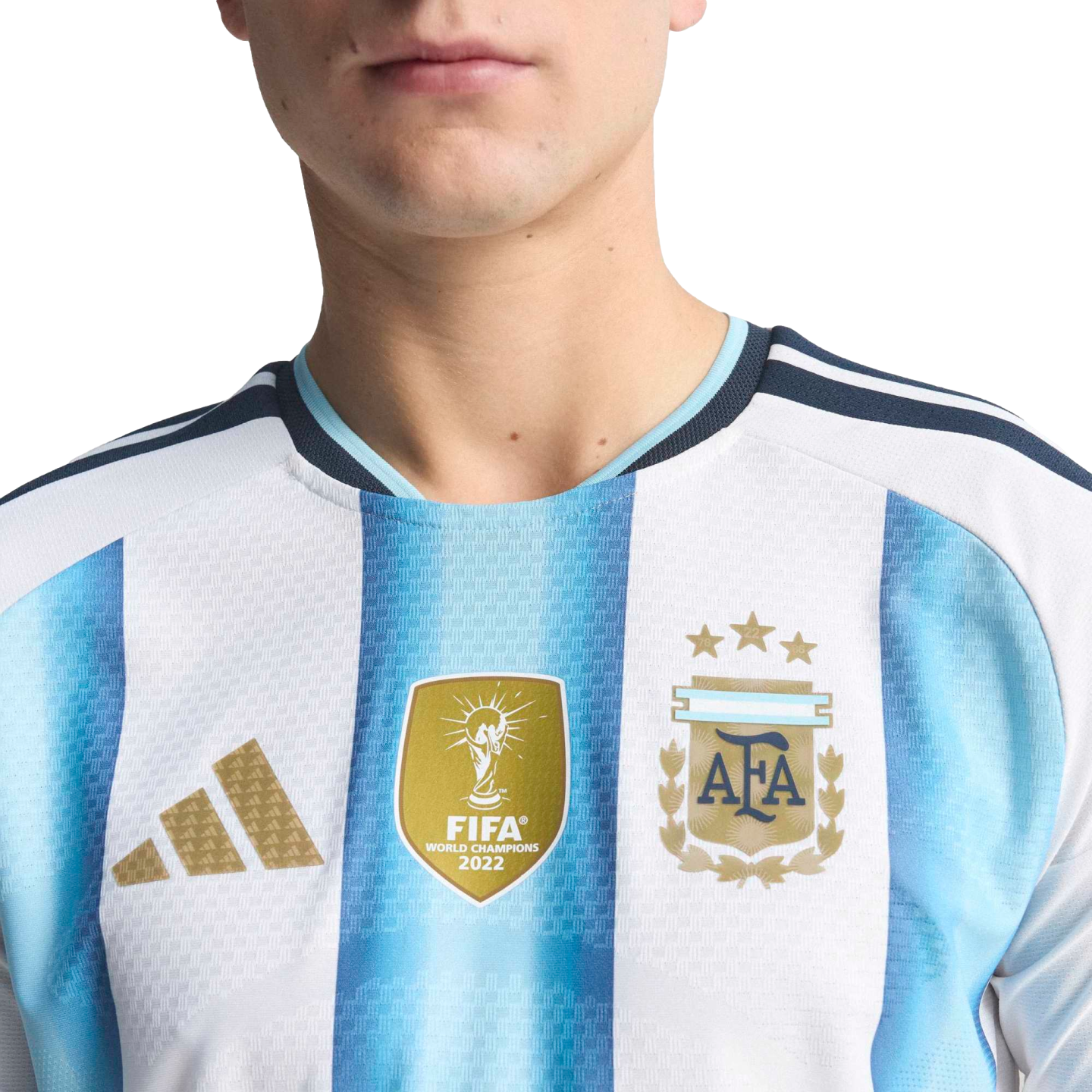Close-up of Argentina's home jersey with light blue and white stripes, featuring the golden FIFA World Champions 2022 patch and the AFA crest with three stars.