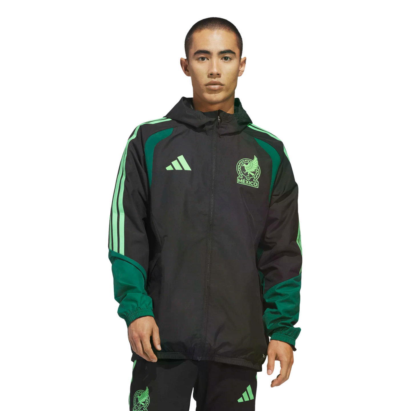 A man wearing a black and green Adidas Mexico National Team windbreaker and matching pants stands against a black background. The jacket features light green team and brand logos.
