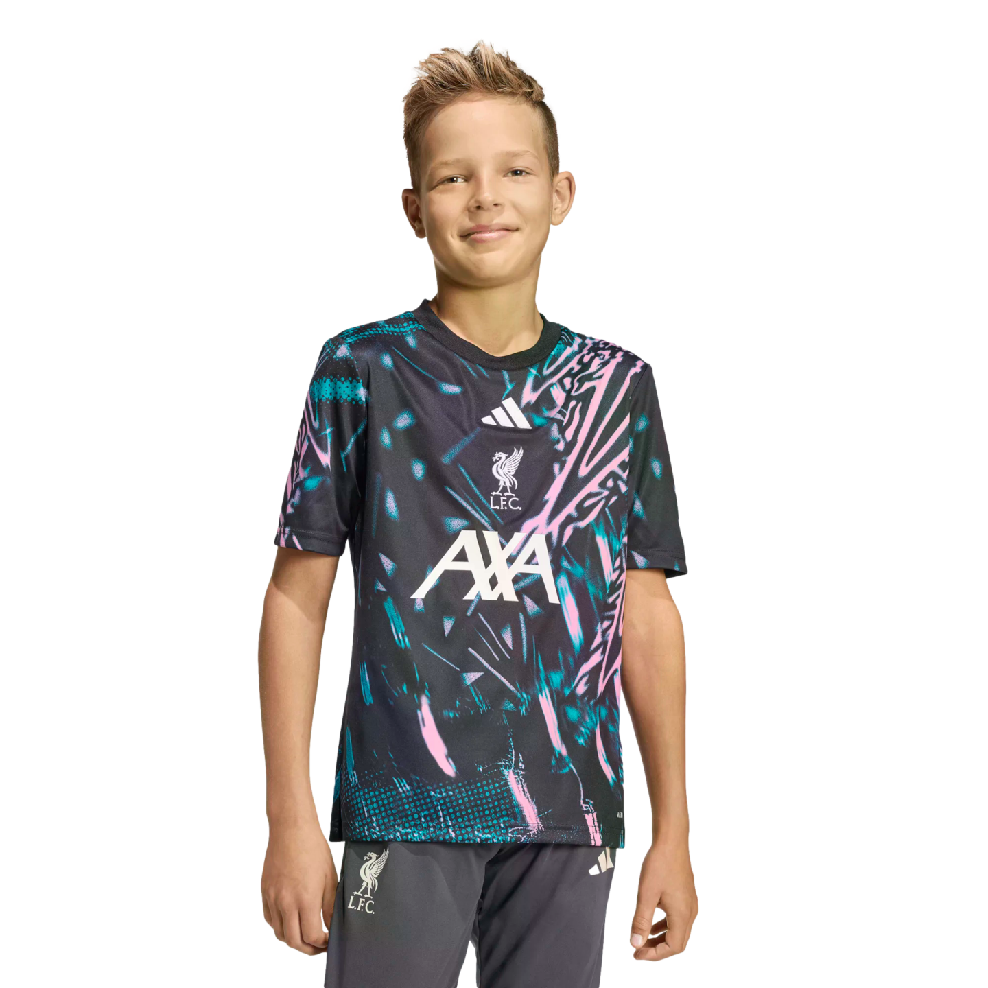 A young boy smiling in a dark Liverpool FC training jersey with pink and teal patterns and grey shorts against a black background.