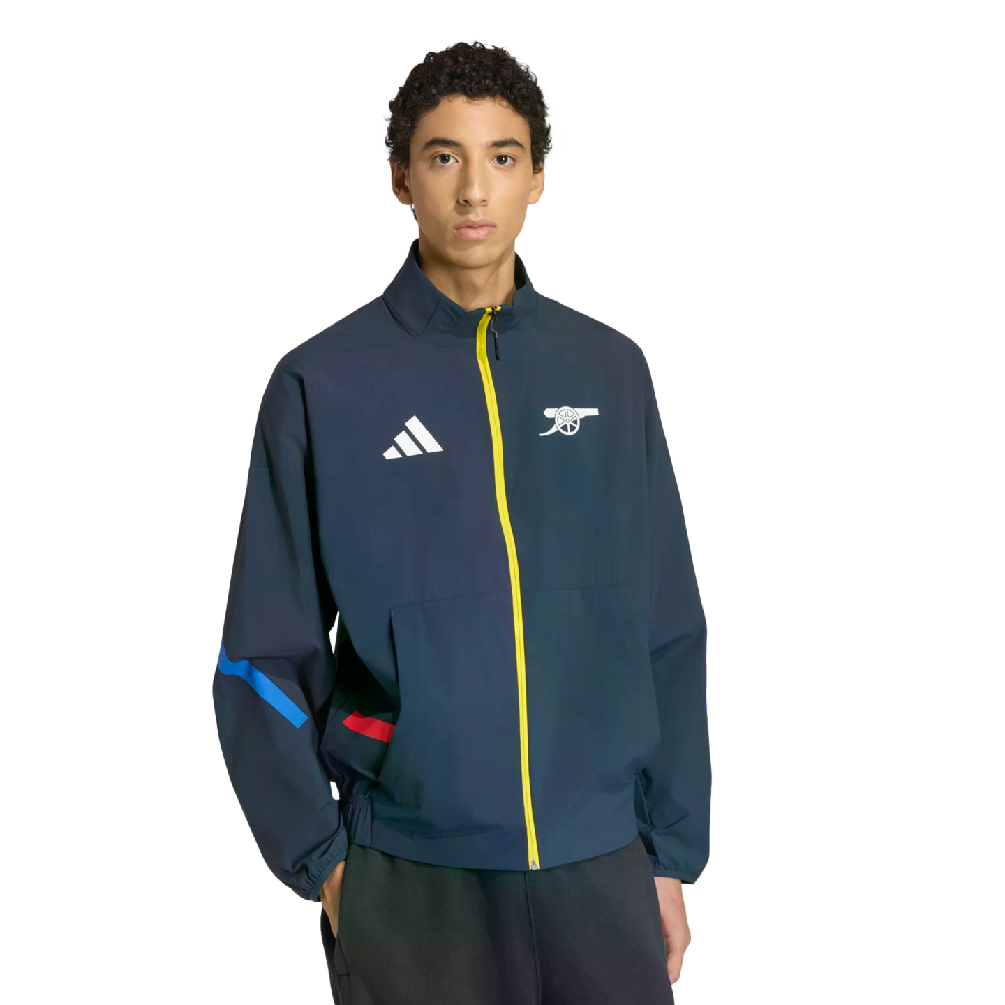 A man wears a navy blue Adidas track jacket with a yellow zipper, featuring a white Adidas logo and the Arsenal FC cannon crest.