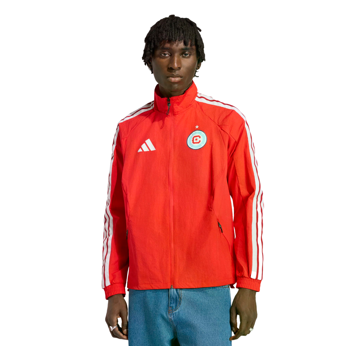 Man wearing a red Adidas track jacket with a Chicago Fire FC crest and blue jeans, standing against a black background.