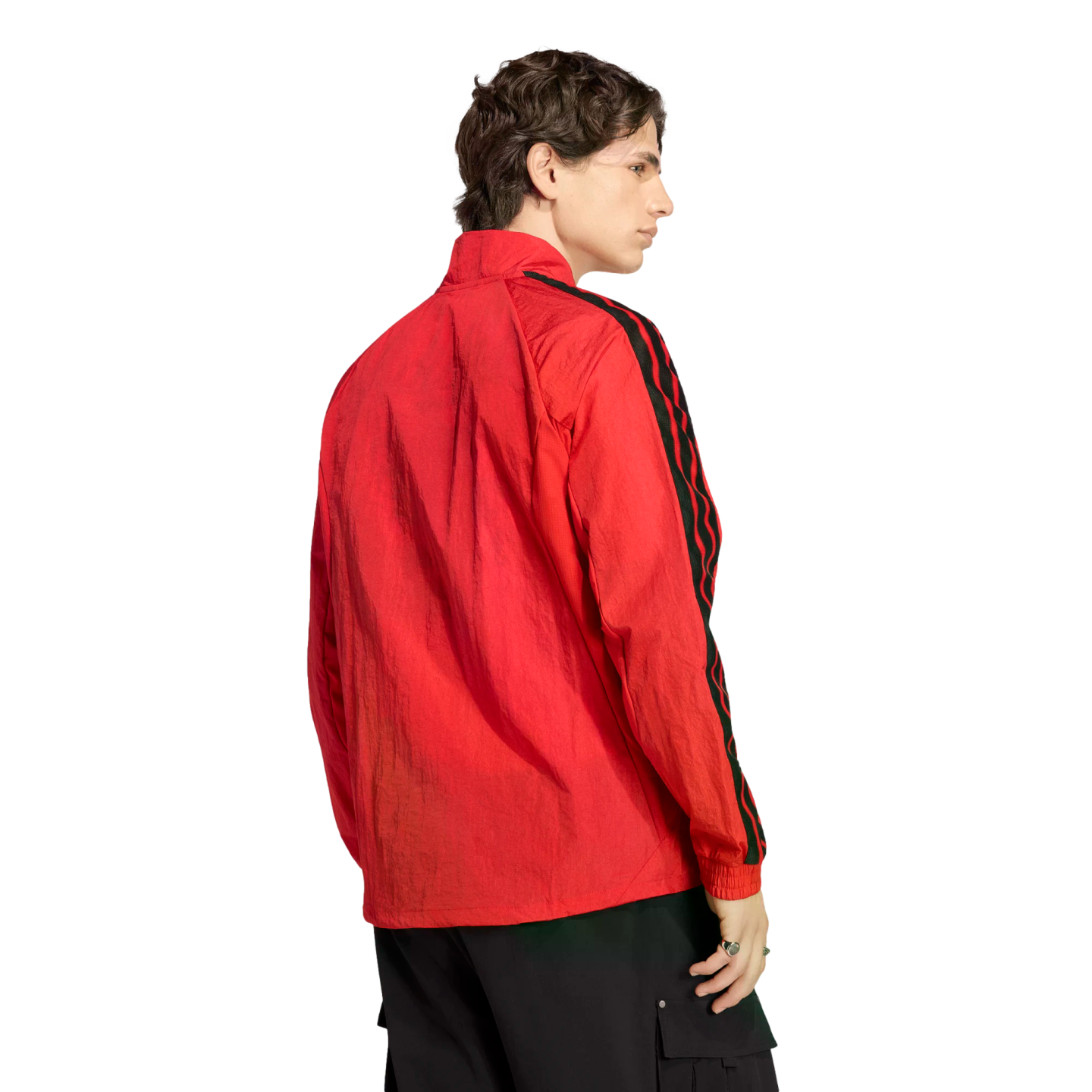 Rear-side view of a man in a red jacket with black patterned stripes on the sleeves and dark cargo pants against a black background.