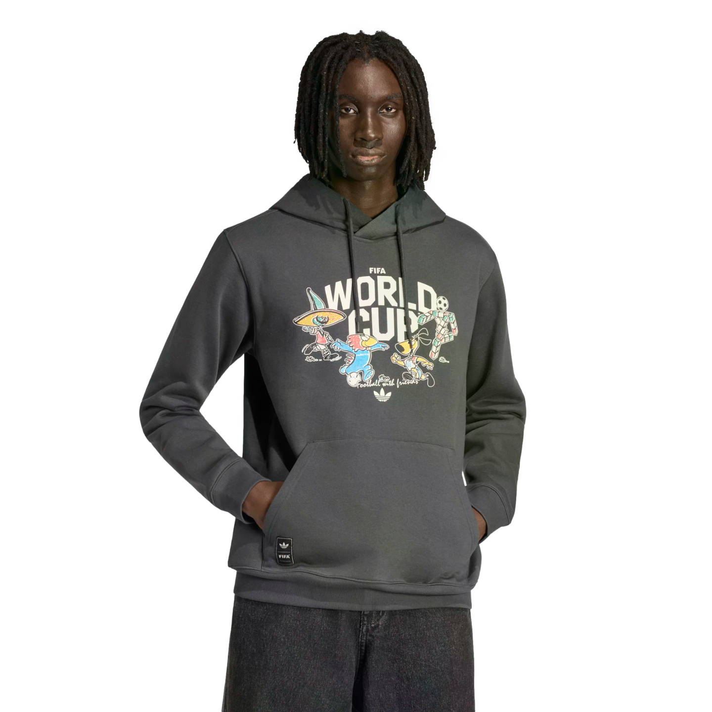 A Black man with dreadlocks wears a grey Adidas FIFA World Cup hoodie with colorful cartoon mascots on the chest, standing against a black background.