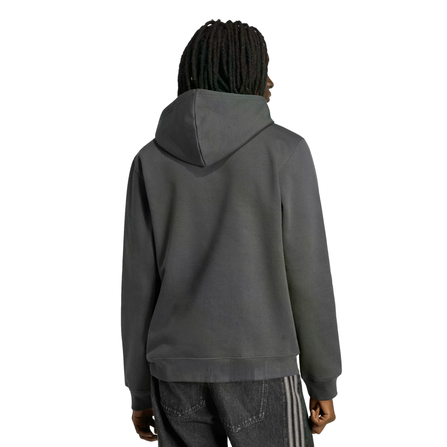 Rear view of a person with dark dreadlocks wearing a dark grey hoodie and black pants with side stripes, standing against a black background.
