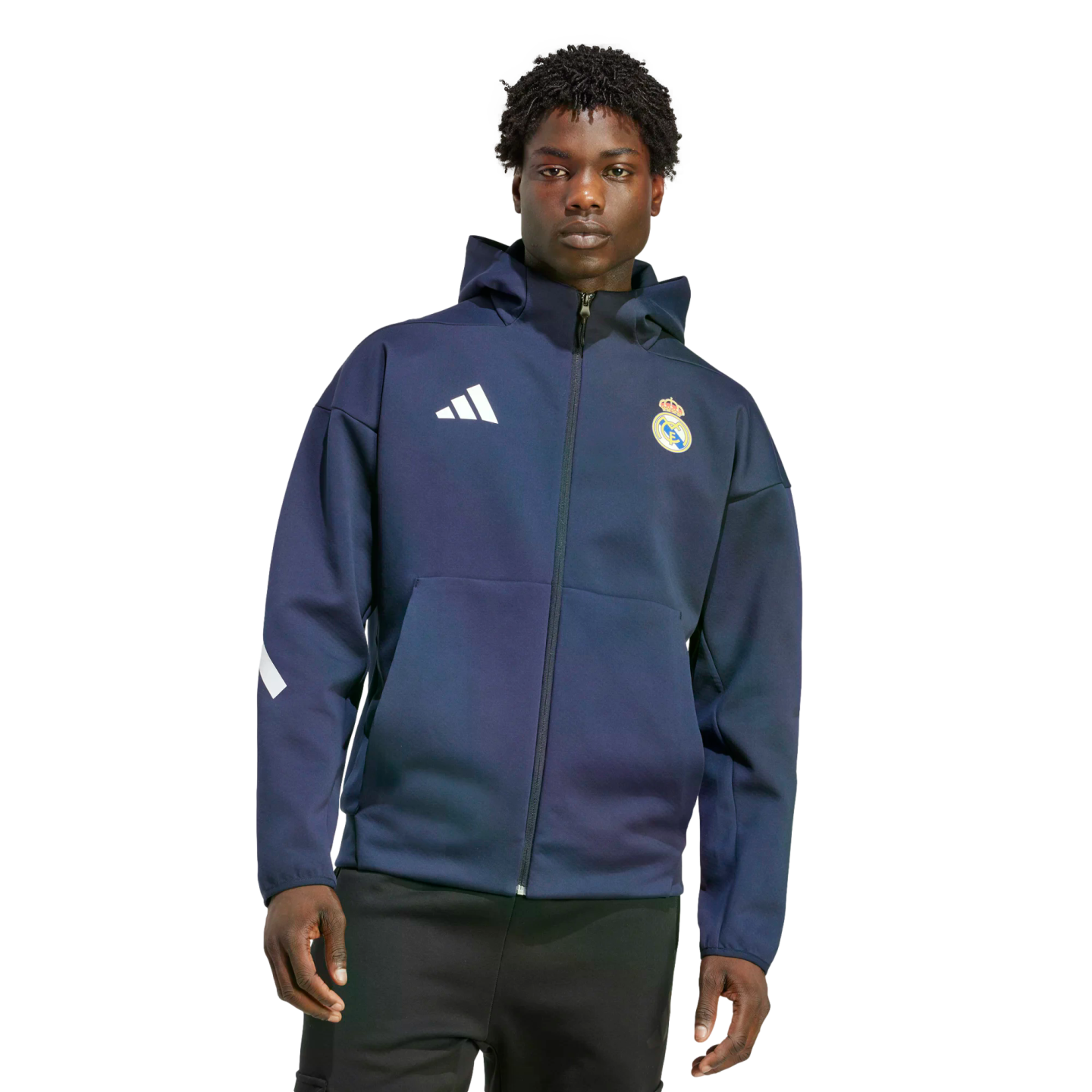 A man wearing a navy blue Adidas Real Madrid zip-up hoodie and black pants, standing against a white background.