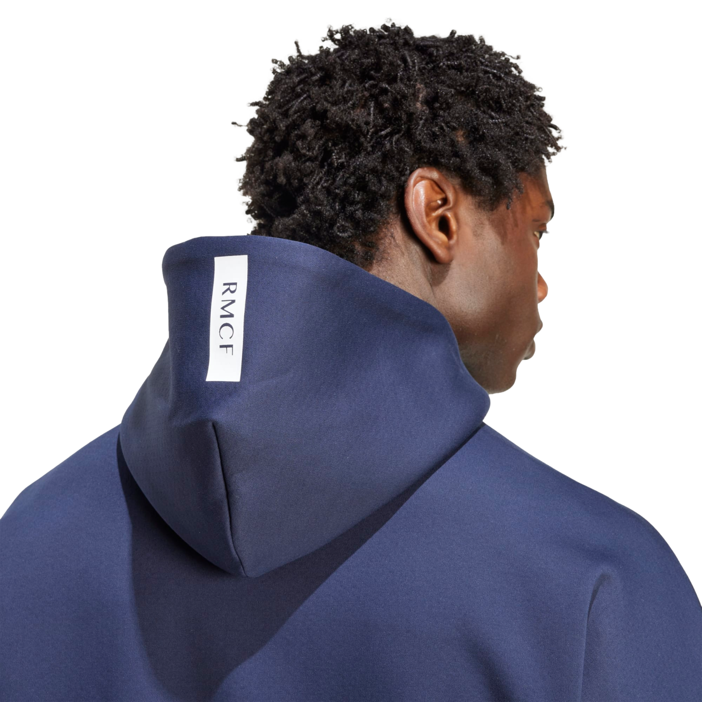 Back view of a man with short curly hair wearing a navy blue hoodie with a vertical white "RMCF" tag on the hood.