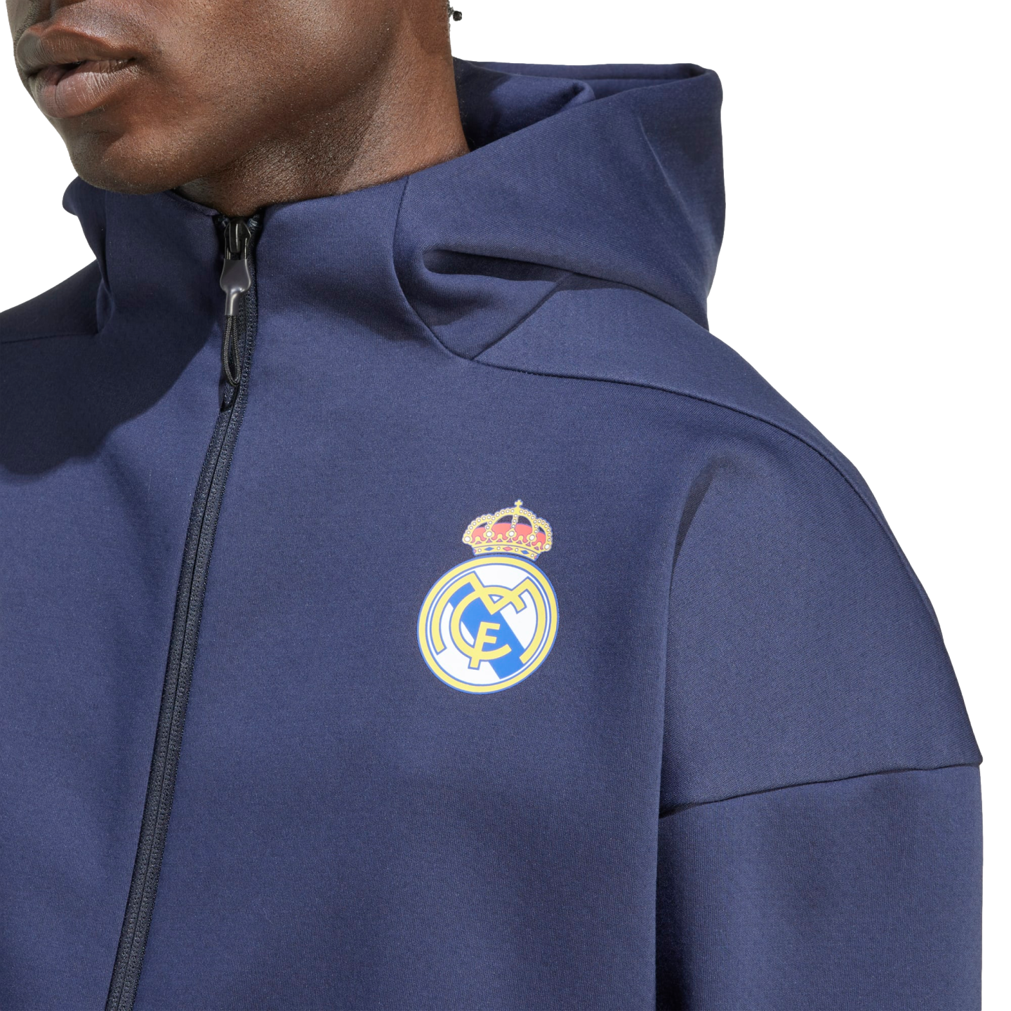 A person wears a navy blue Real Madrid zip-up hoodie with the team's crest prominently displayed on the left chest.