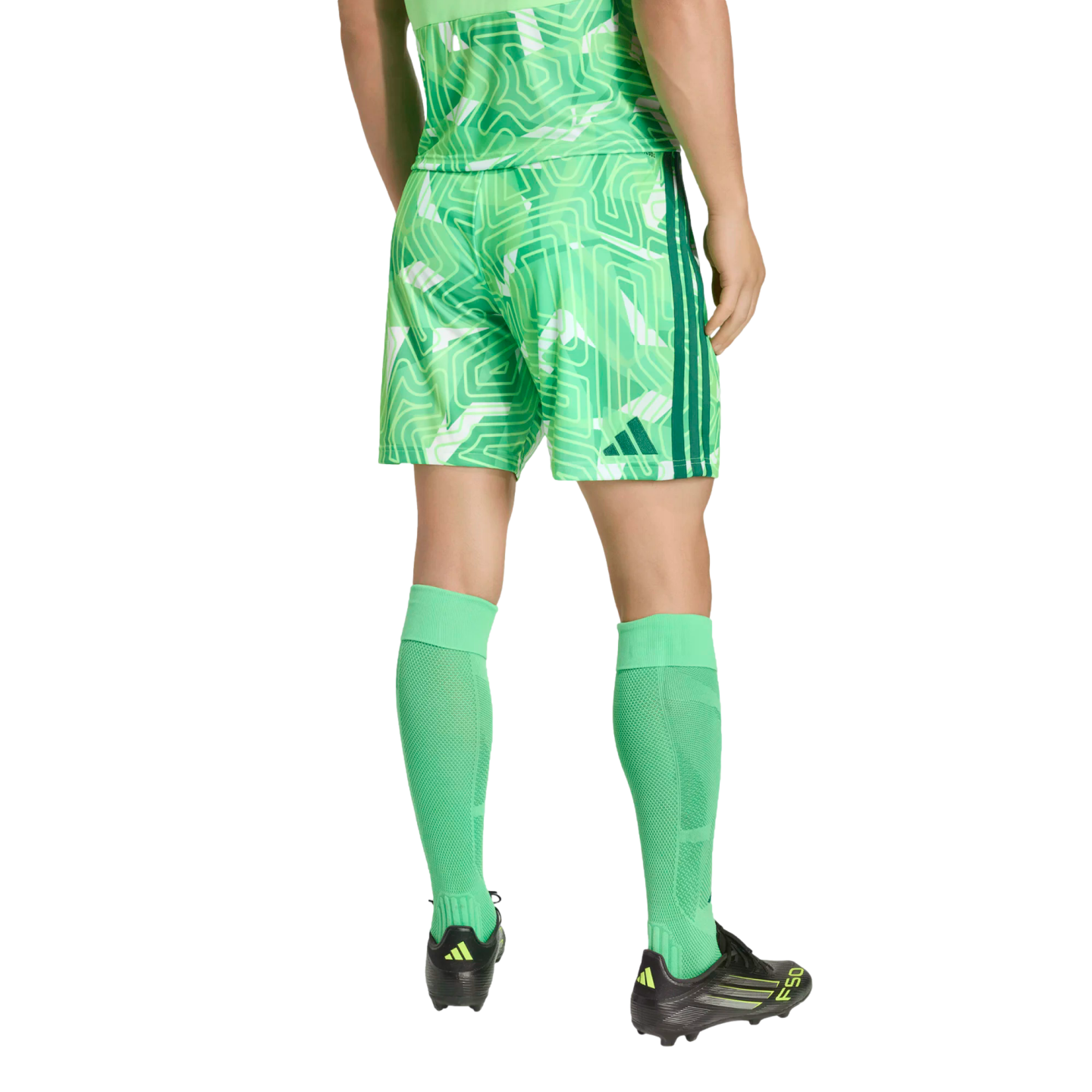 Rear view of a person wearing a green geometric-patterned Adidas soccer uniform, bright green calf-high socks, and black Adidas soccer cleats against a black background.