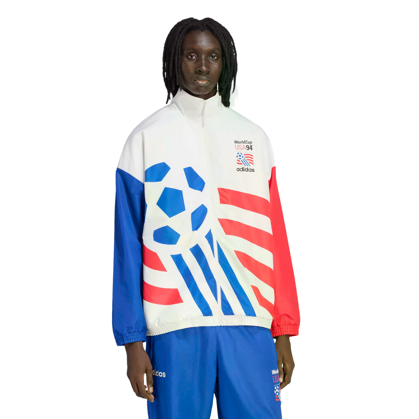 A man with dreadlocks wearing a white Adidas tracksuit jacket with red and blue graphics commemorating World Cup USA '94. The jacket features a large blue soccer ball design, red stripes, and mismatched red and blue sleeves. He is wearing coordinating blu