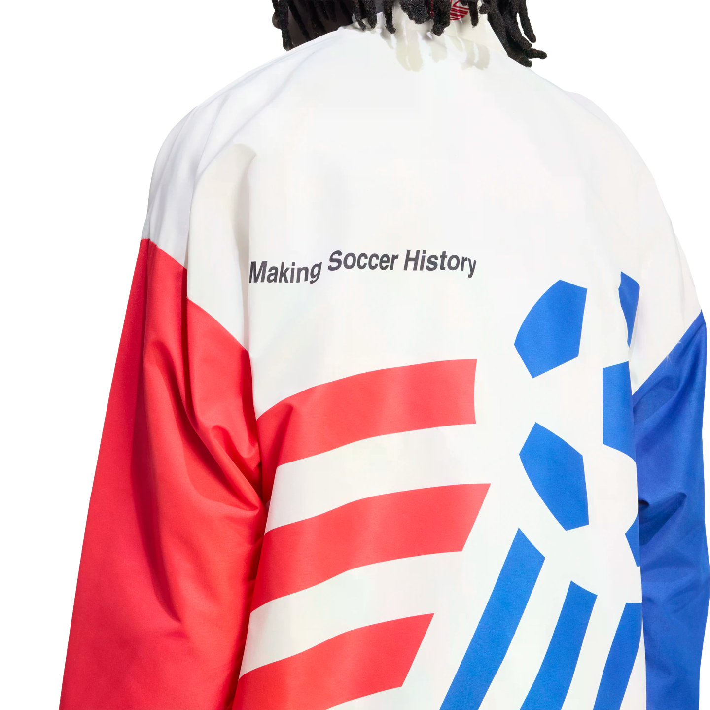 A close-up view from behind of a person wearing a white, red, and blue athletic jacket against a black background. The text "Making Soccer History" is printed in black on the white upper back. The lower back features red horizontal stripes on the left and