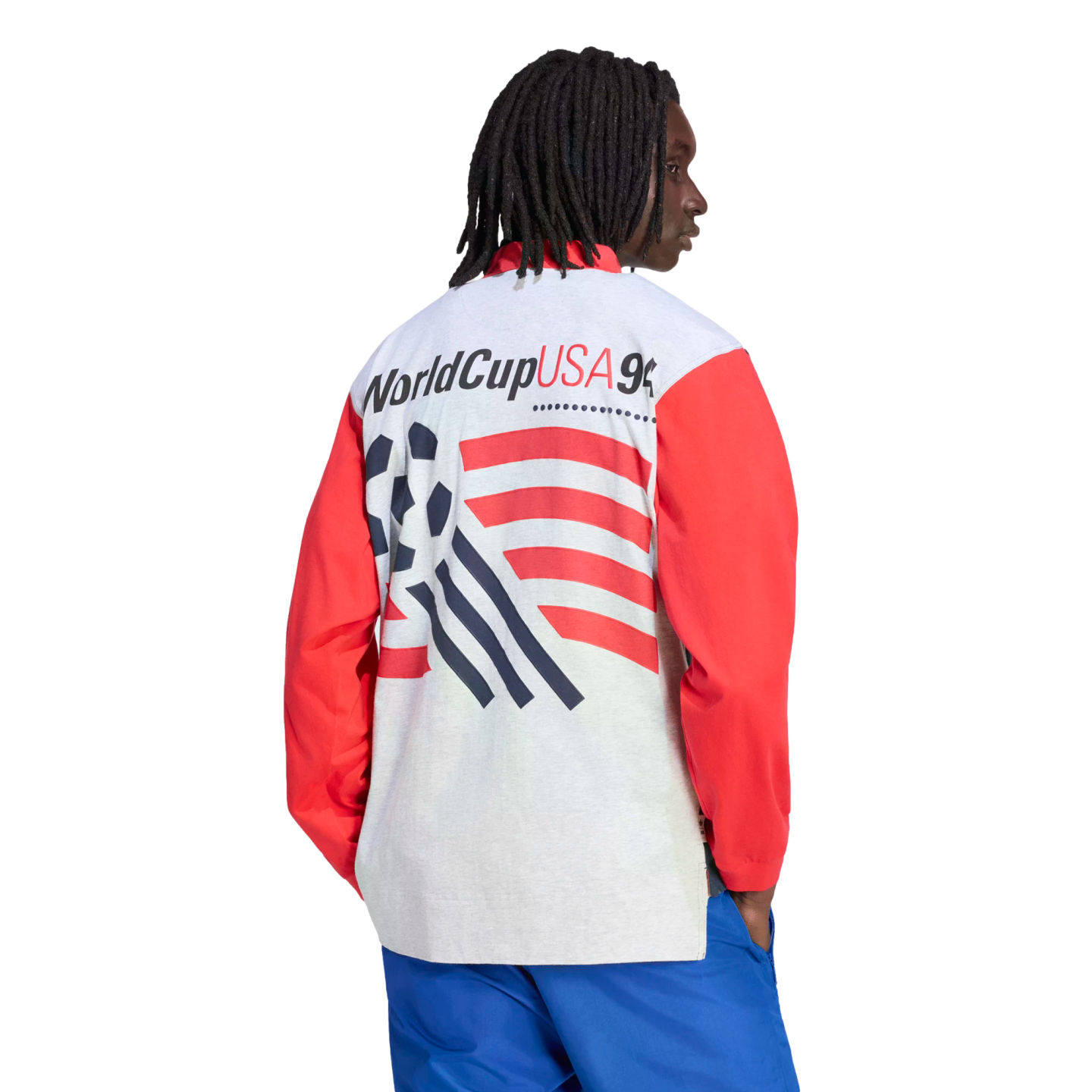 A rear-view shot of a person with long dreadlocks wearing a white long-sleeved shirt with red sleeves and blue pants against a black background. The back of the shirt features the "WorldCupUSA94" logo above a graphic of a soccer ball and red stripes.