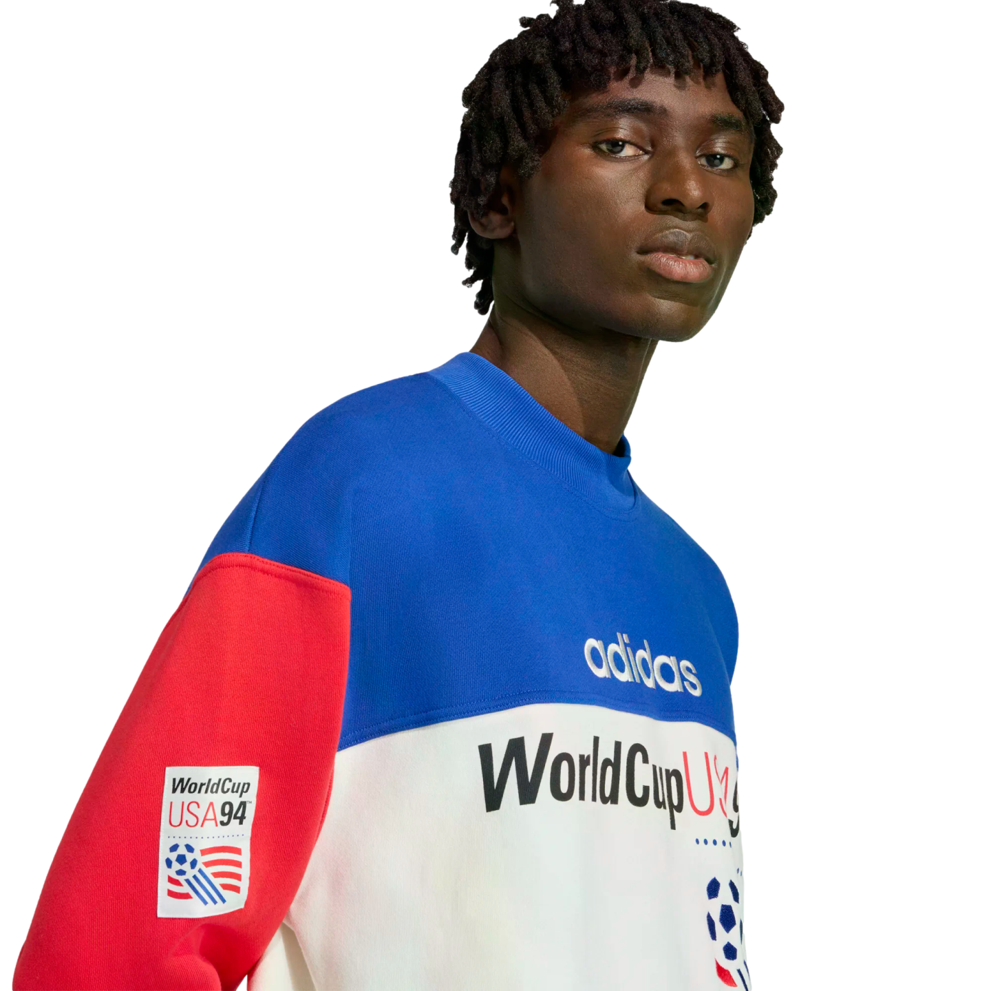 A close-up portrait of a man wearing a blue, white, and red color-blocked Adidas World Cup USA '94 sweatshirt against a solid black background.