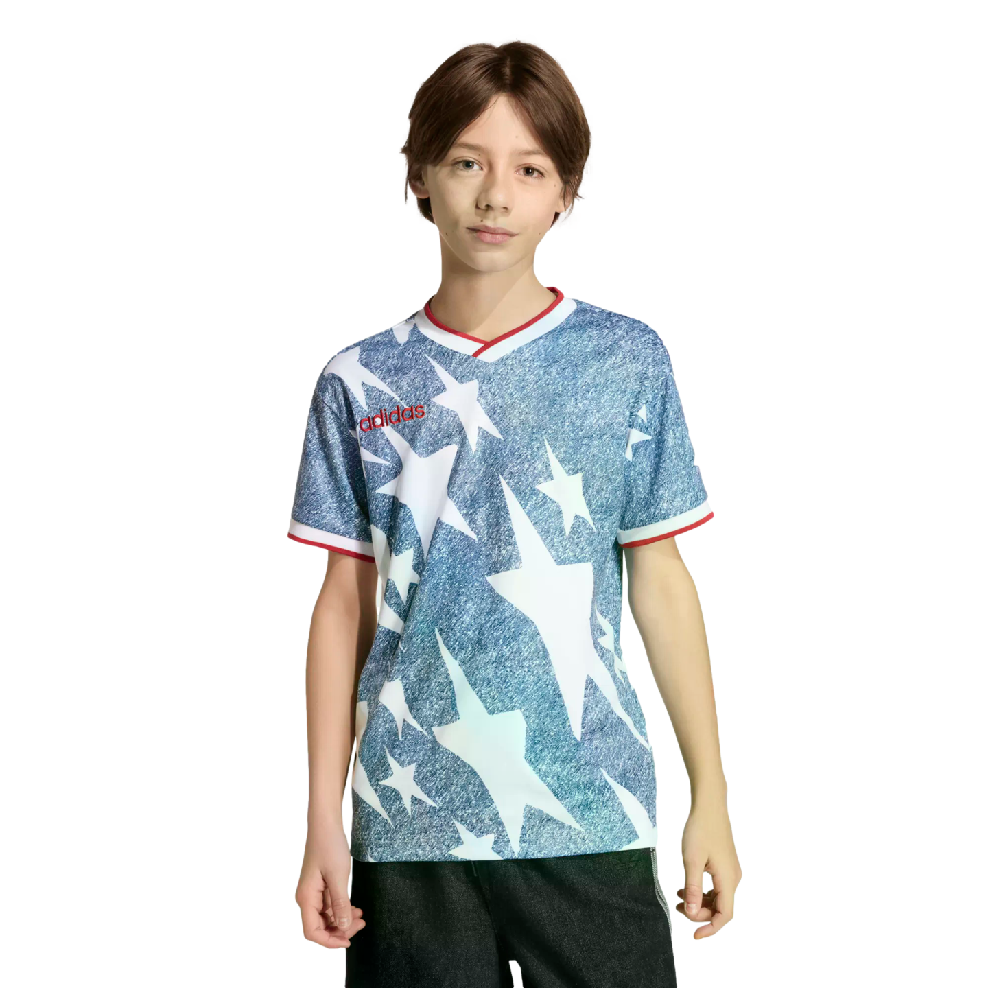 A young person wearing a blue and white star-patterned Adidas shirt with red trim and black shorts, standing against a black background.