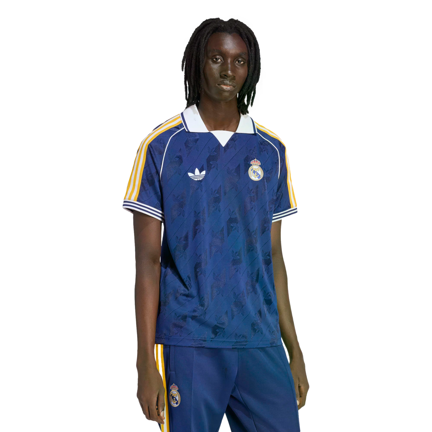 A person with dreadlocks wearing a navy blue Real Madrid soccer jersey and matching track pants against a black background.