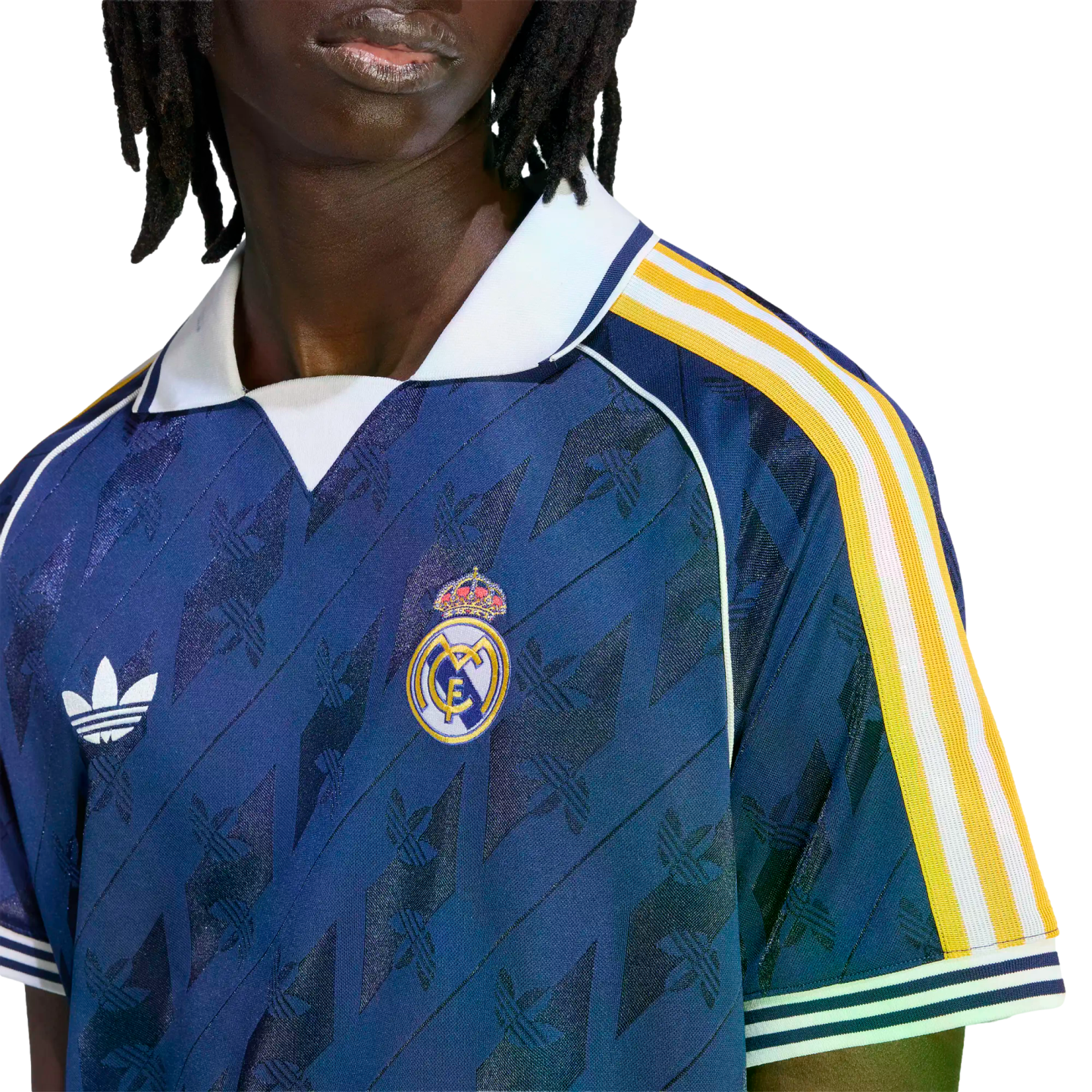 Close-up of a person wearing a navy blue Adidas Real Madrid soccer jersey with white and yellow sleeve stripes and a white polo collar.
