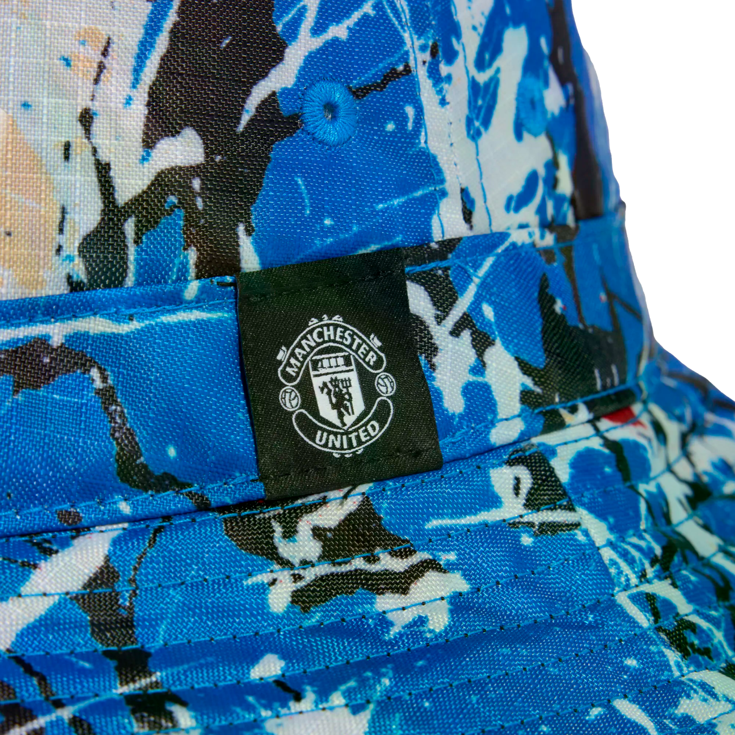 Close-up of a blue and white splash-patterned bucket hat featuring a black label with the white Manchester United crest.