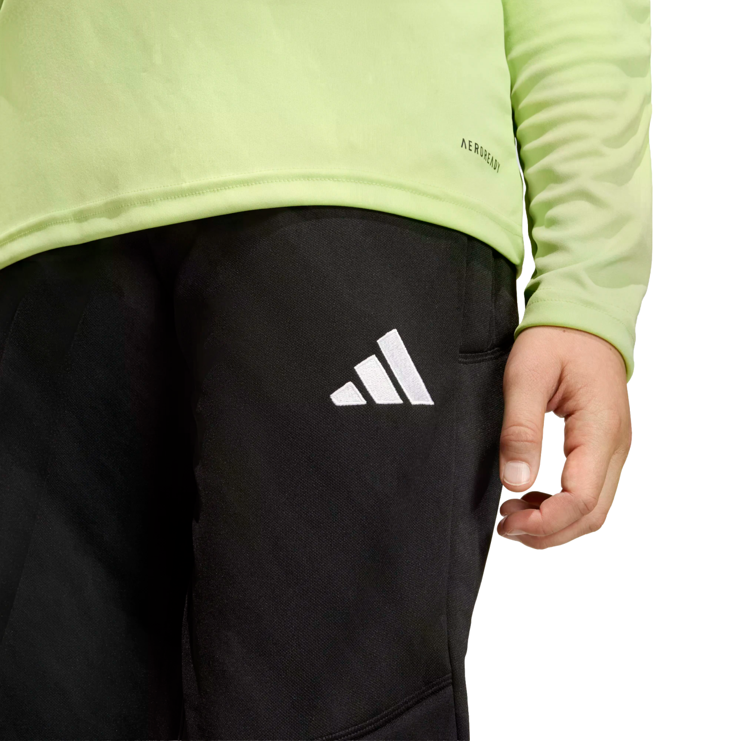A person wearing a lime green long-sleeved shirt and black athletic pants with a white Adidas logo on the thigh.