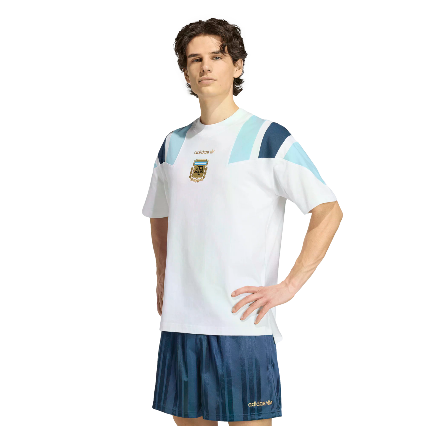 A man wears a white Adidas Argentina t-shirt and blue shorts, posing against a white background.