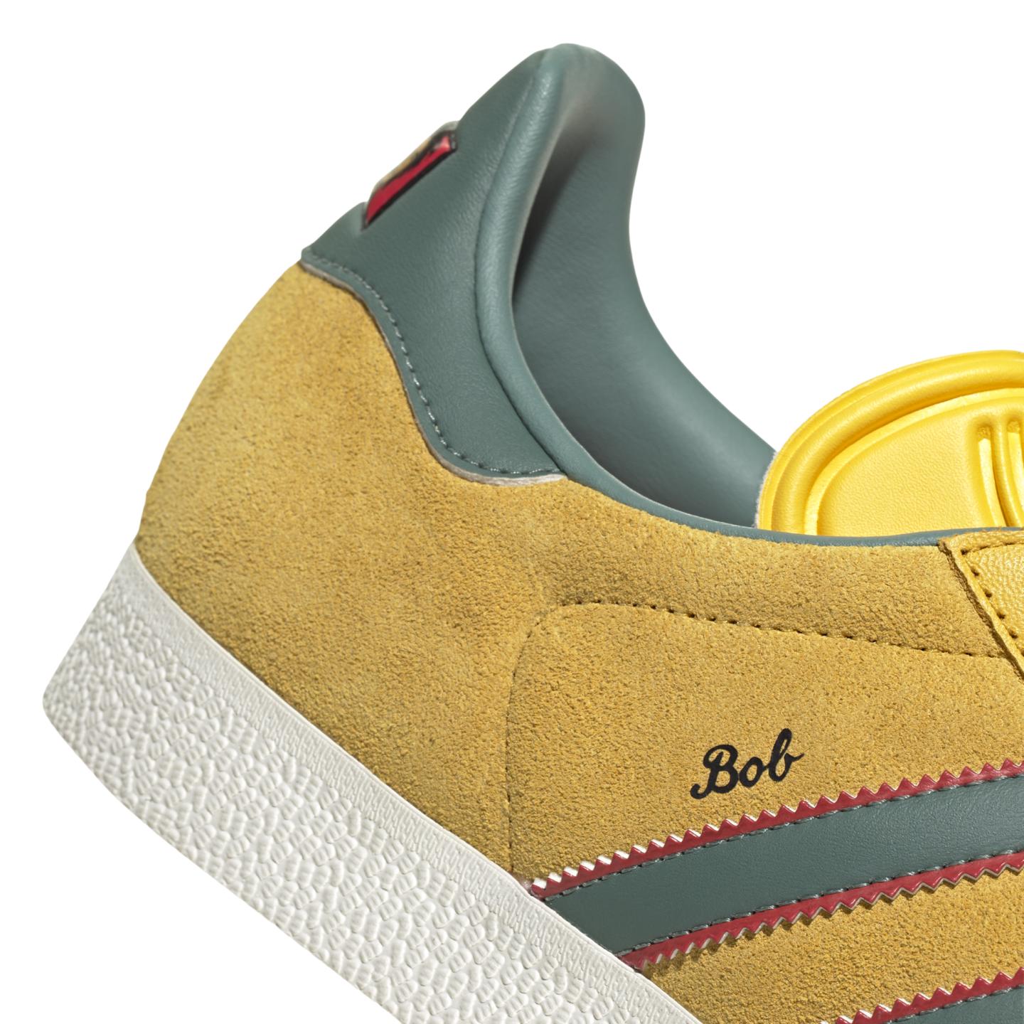 Close-up of a yellow suede sneaker featuring teal stripes with red serrated edges and the name "Bob" in cursive script.
