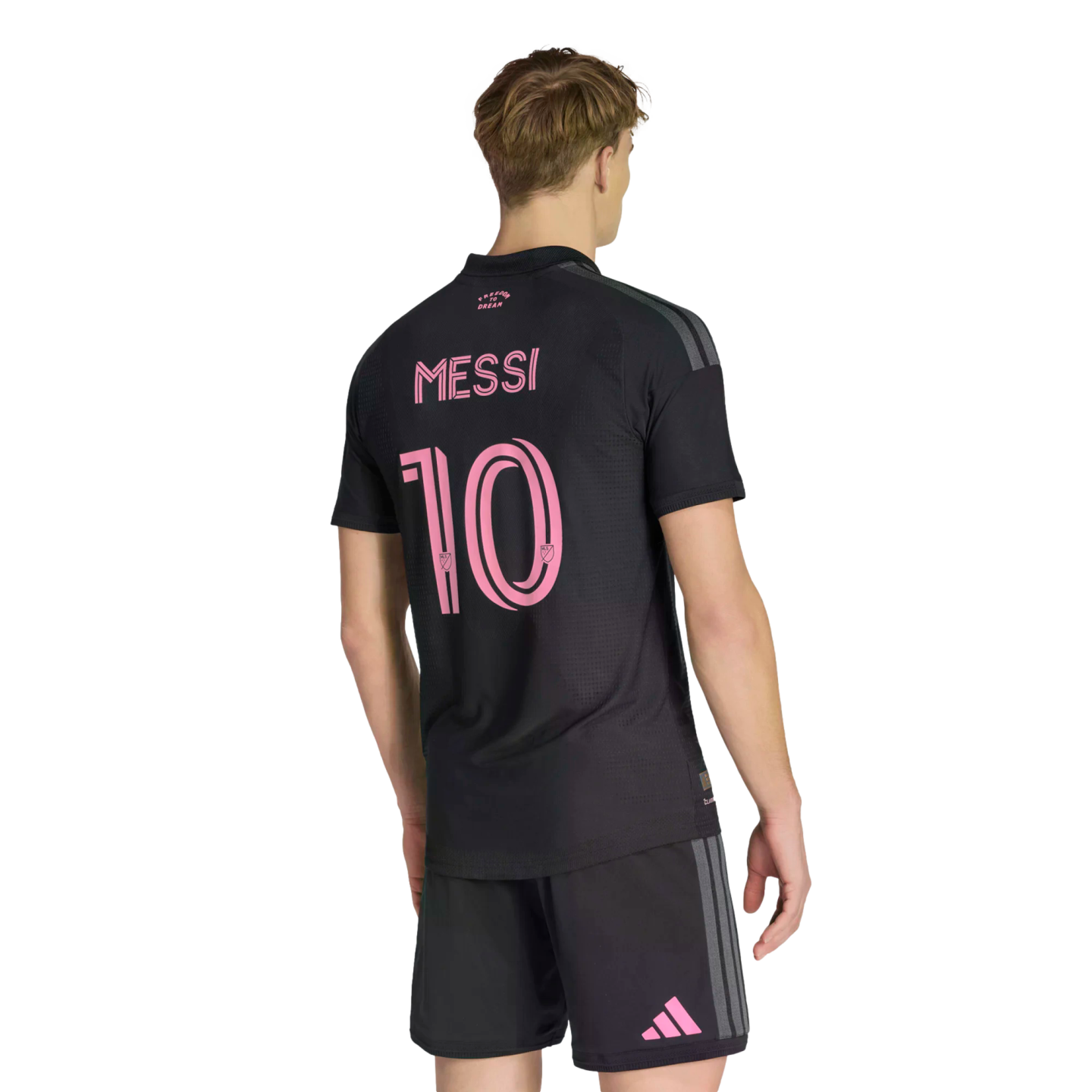 A person from behind wearing a black soccer jersey with the name "Messi" and the number "10" in pink on the back. He also wears matching black shorts with a pink Adidas logo on the leg, all set against a solid black background.