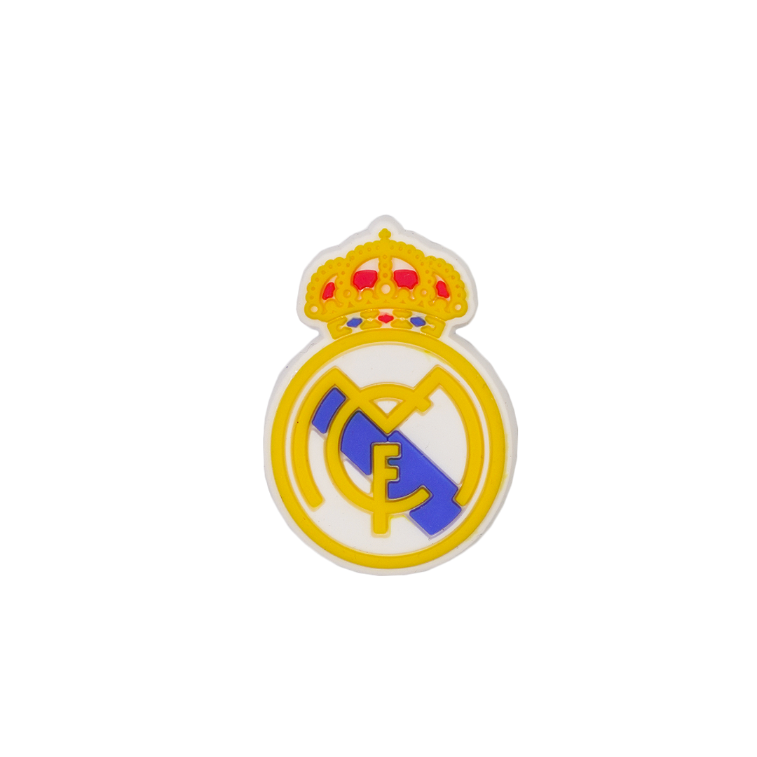 Soccer Croc charm featuring the Real Madrid football club crest with a yellow and white circular logo, a gold crown on top, and stylized blue and yellow lettering in the center.
