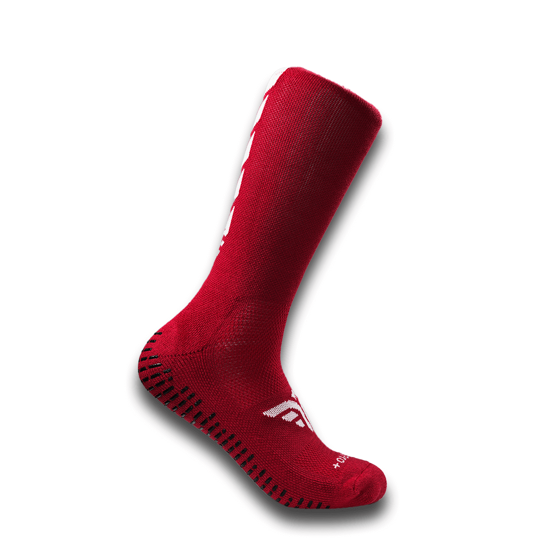 A studio shot of the For The Footballer XLR8R Pro No Slip Socks - Red, a high-cut athletic sock featuring black rectangular non-slip grips along the sole and heel, a white logo on the top of the foot, and a ribbed texture on the upper leg.