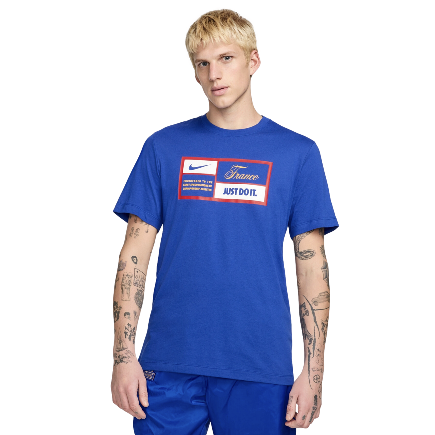 A man with blond hair and arm tattoos wearing a royal blue Nike France graphic t-shirt and matching blue shorts, isolated against a white background.