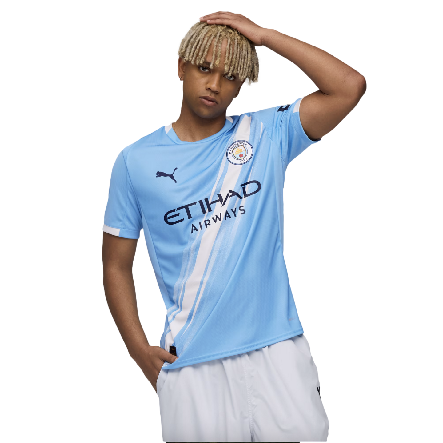 A young man with blonde dreadlocks wears a blue Manchester City soccer jersey and white shorts against a white background.