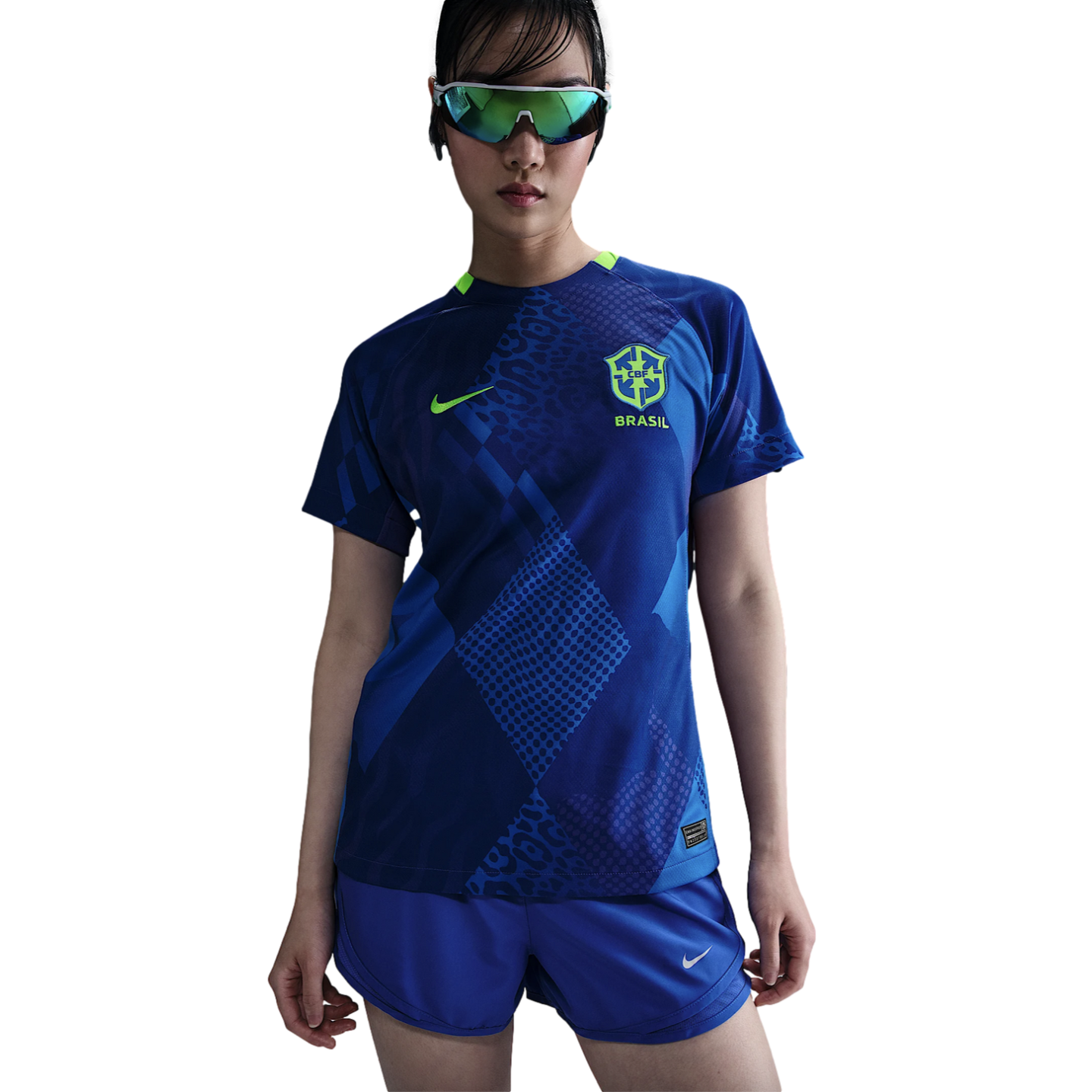 A person wears a blue Nike Brazil national team soccer jersey with leopard print patterns, matching shorts, and iridescent sports sunglasses against a white background.