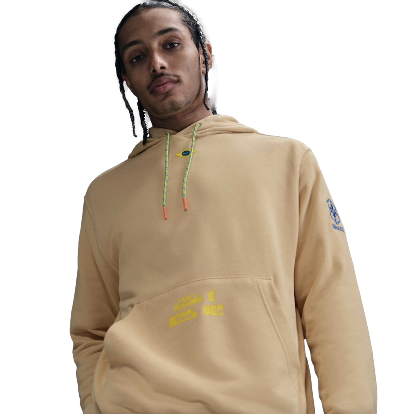 A man with braids wearing a tan hoodie with the Brazilian football team crest on the sleeve and yellow text on the front pocket.