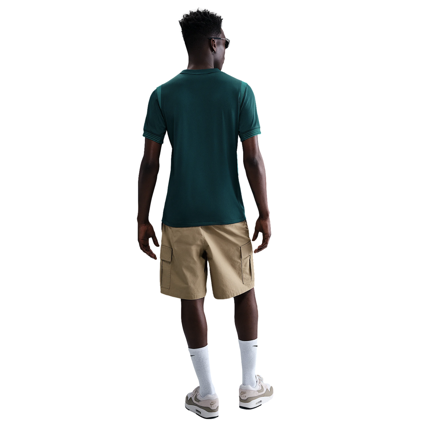 Back view of a man wearing a dark green t-shirt, tan cargo shorts, white crew socks, and beige sneakers against a white background.