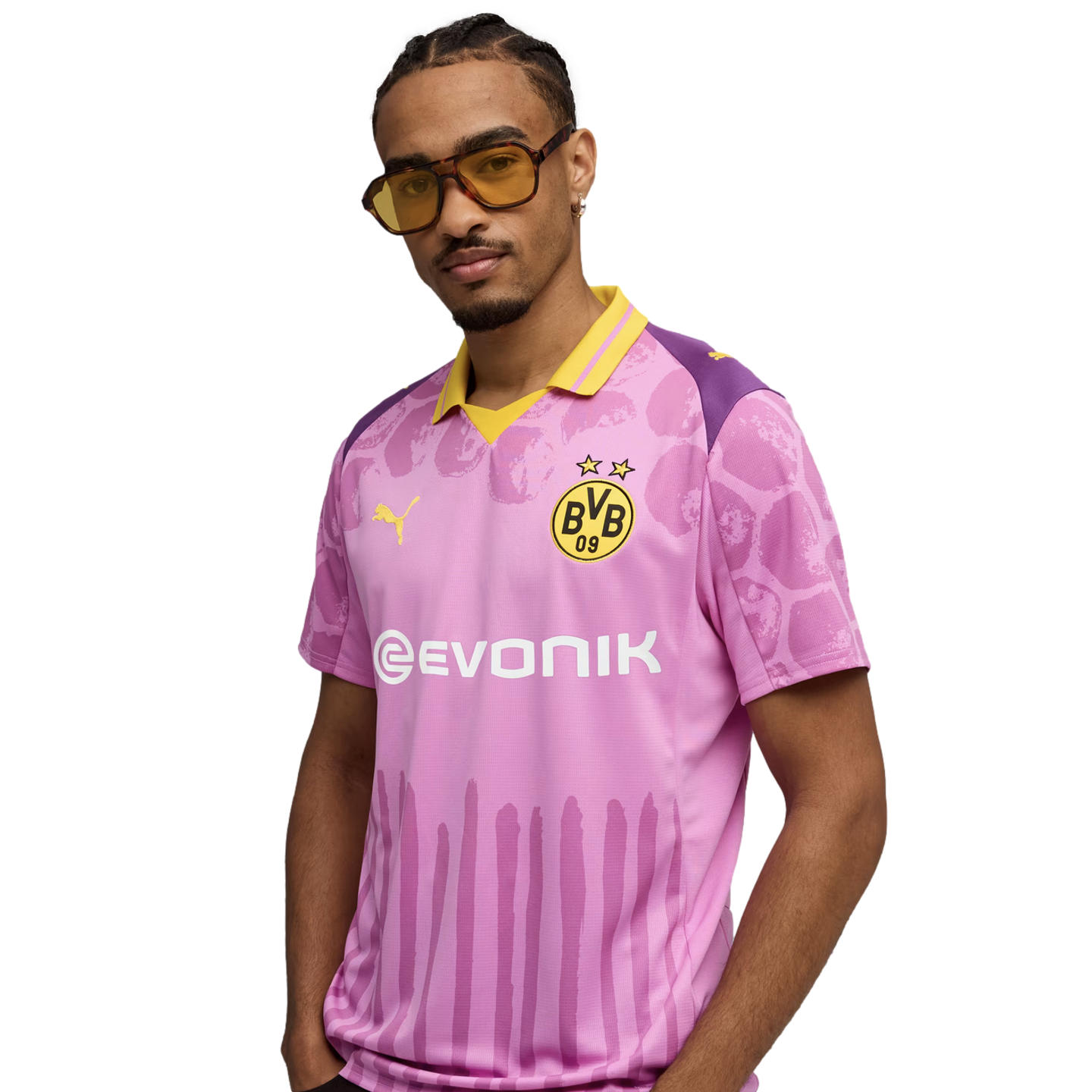 A man wearing yellow-tinted sunglasses poses in a pink and purple Borussia Dortmund soccer jersey with yellow accents.