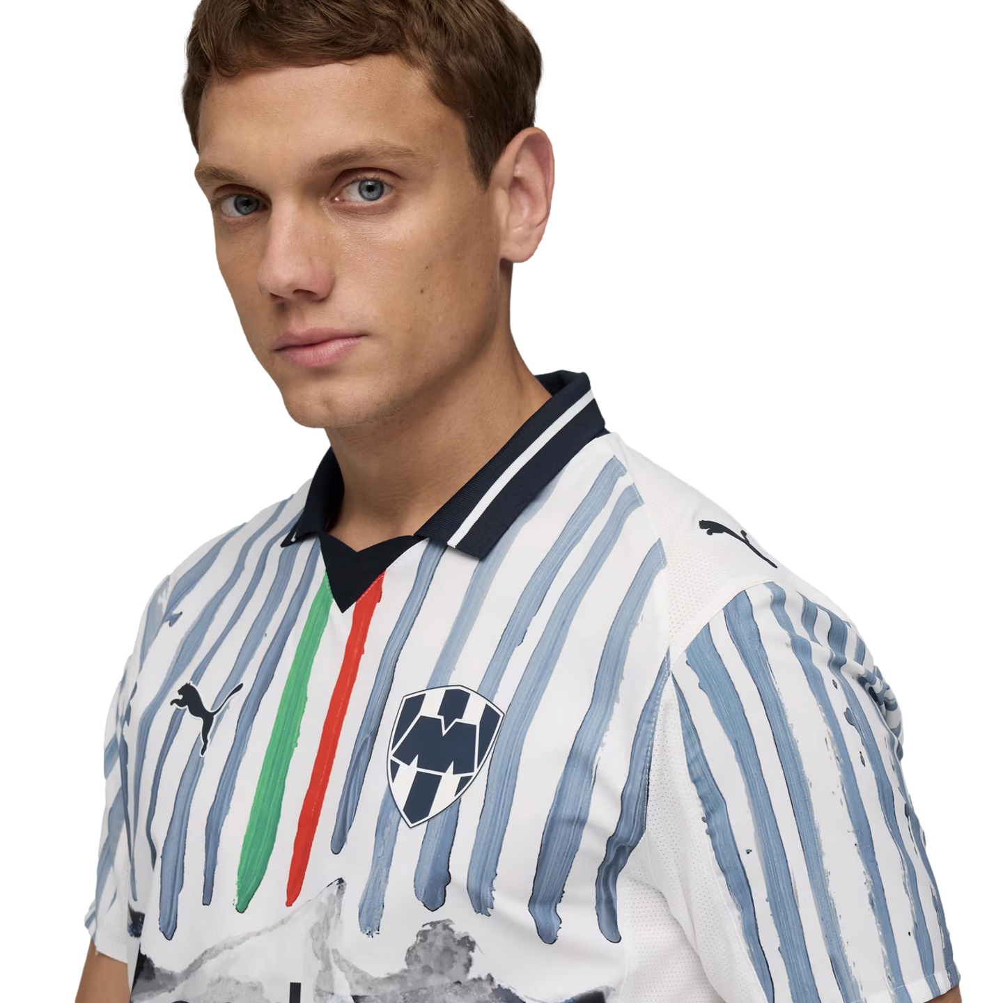 A man in a white Puma football jersey featuring light blue brushstroke stripes, a central green and red stripe, and the Monterrey club crest.