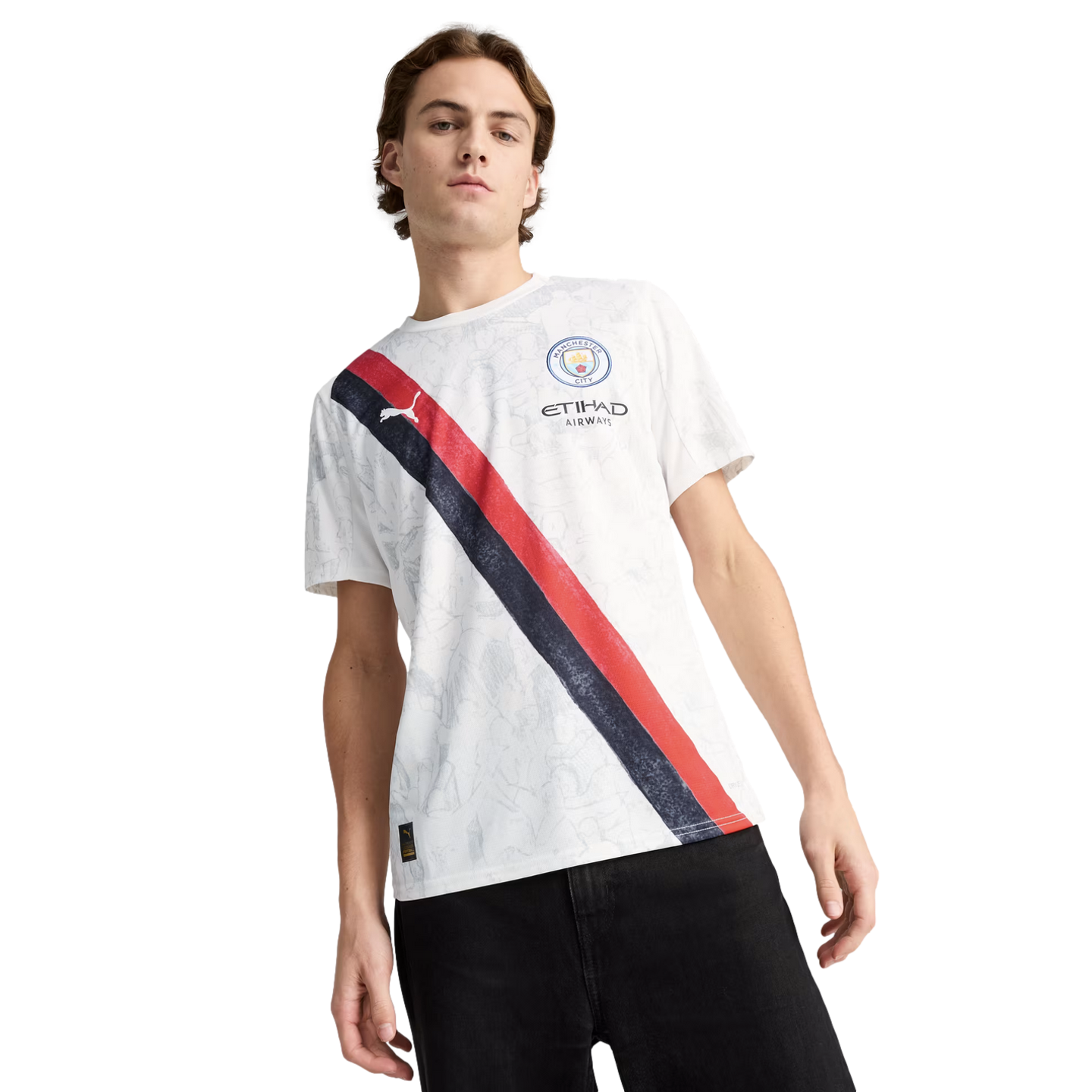 A man wearing a white Manchester City jersey with a navy and red diagonal stripe and black pants, standing against a white background.