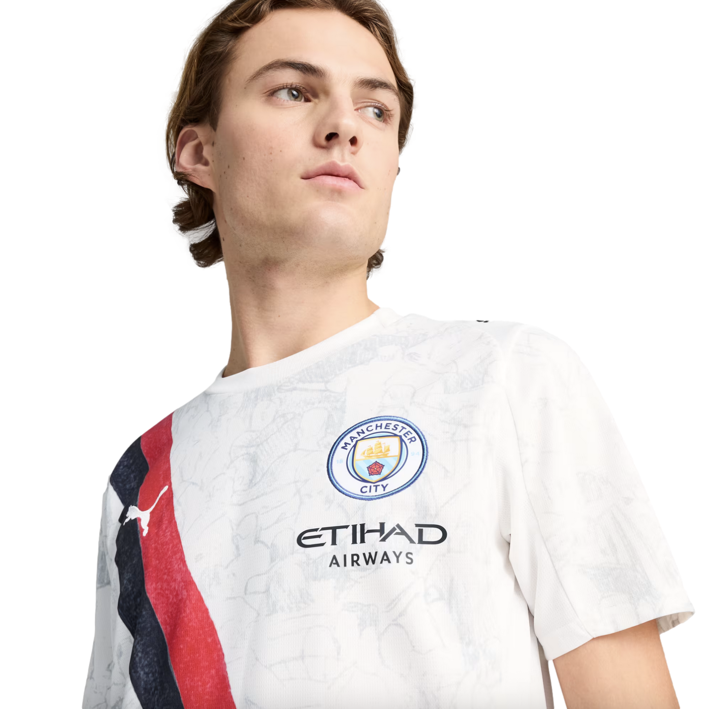 A young man looking to the side while wearing a white Manchester City jersey featuring a red and blue diagonal sash.